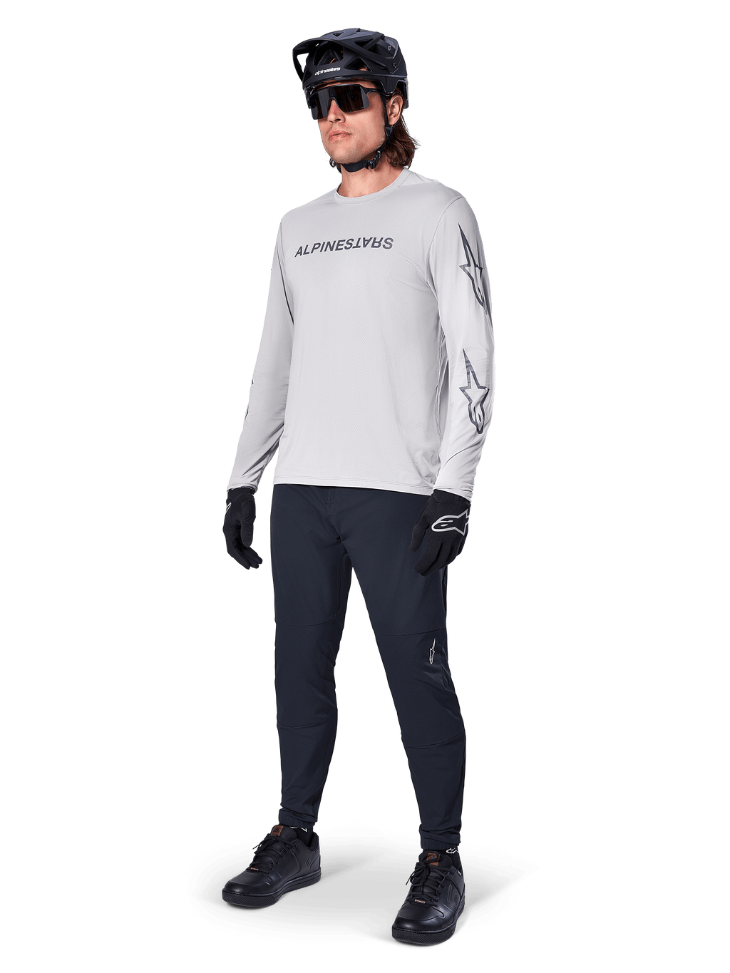 Maglia a maniche lunghe Alpinestars A-Dura Switch, Grigio Chiaro, indossata da un ciclista con pantaloni da mountain bike neri e casco, con logo wordmark nero sul petto e grafiche a stella sulle maniche, abbigliamento tecnico per ciclismo fuoristrada