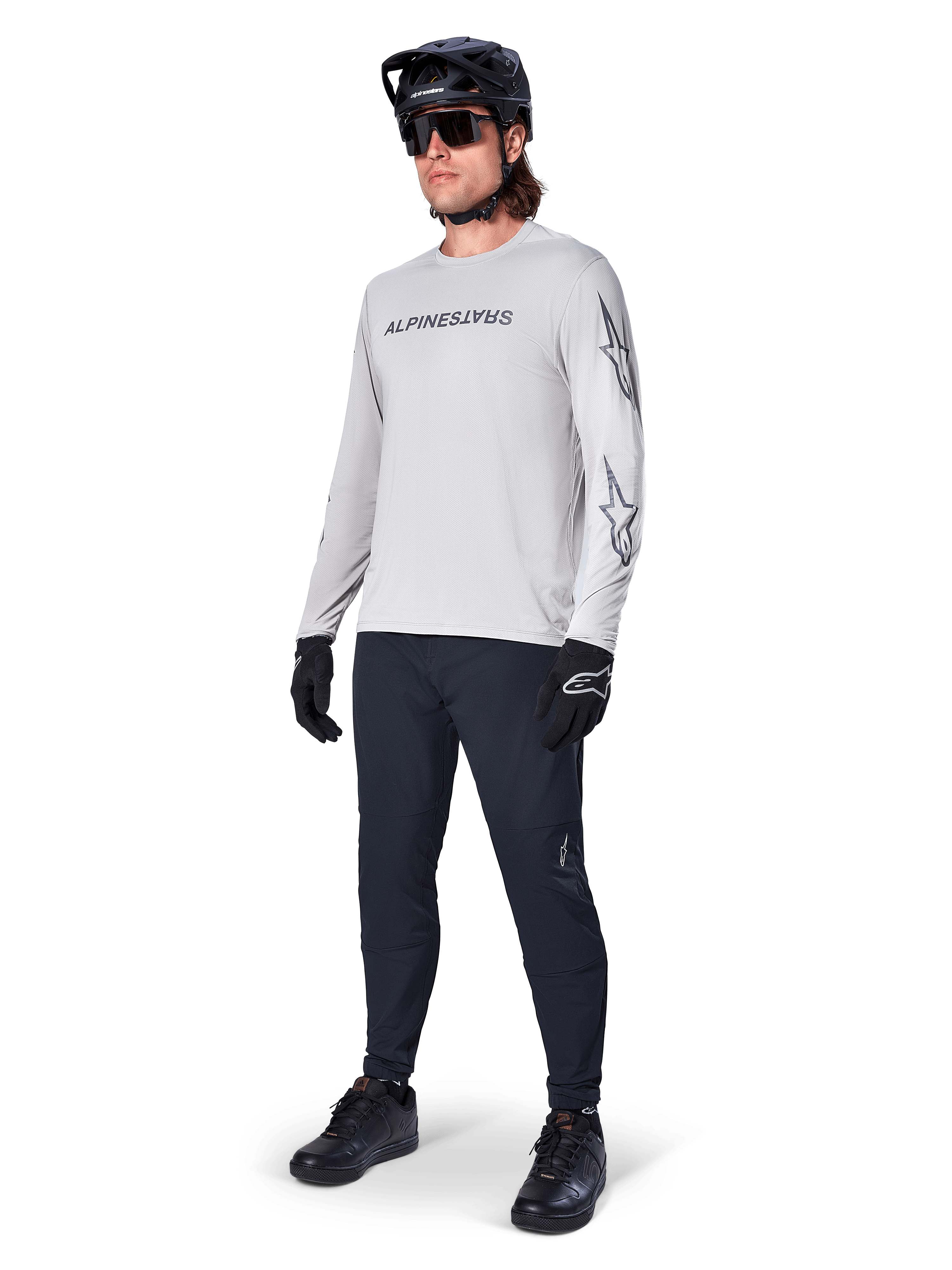 Maglia a maniche lunghe Alpinestars A-Dura Switch, Grigio Chiaro, indossata da un ciclista con pantaloni da mountain bike neri e casco, con logo wordmark nero sul petto e grafiche a stella sulle maniche, abbigliamento tecnico per ciclismo fuoristrada