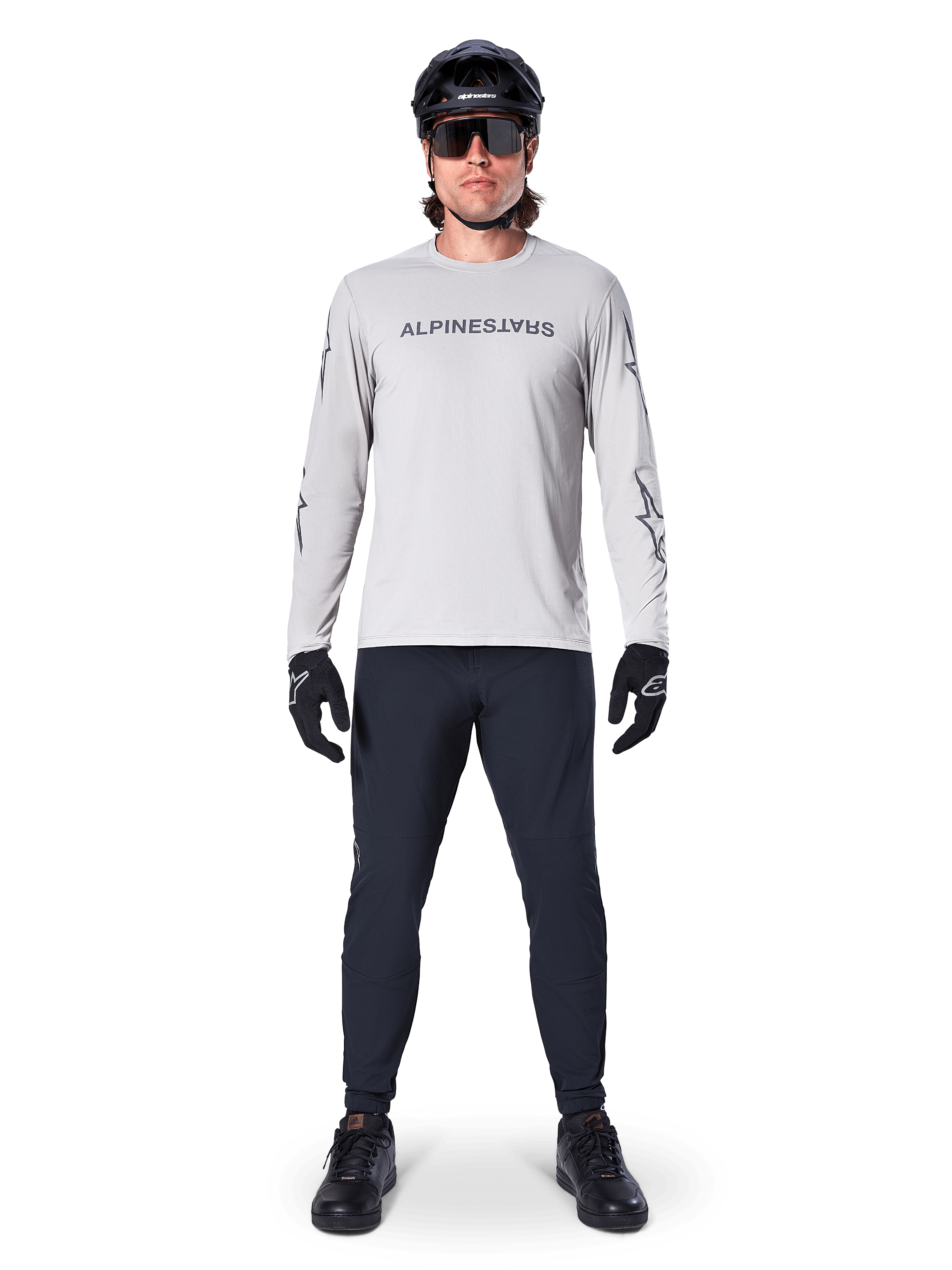 Maglia a maniche lunghe Alpinestars A-Dura Switch in grigio chiaro, con logo wordmark stilizzato sul petto, indossata con pantaloni neri, casco e guanti, abbigliamento tecnico da mountain bike per ciclismo off-road