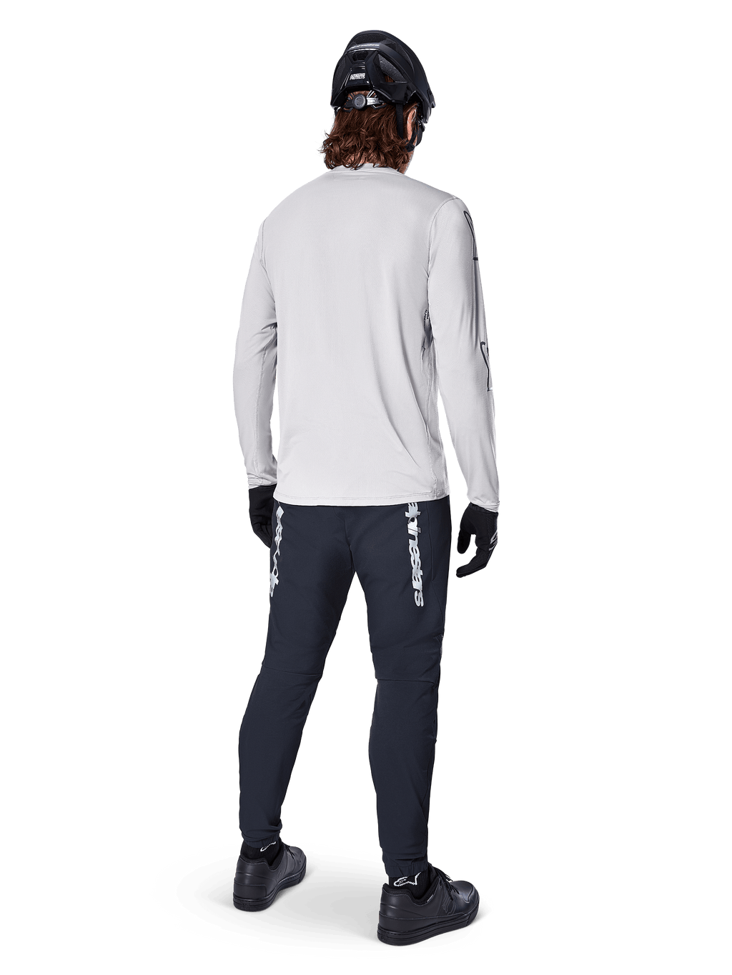 Maglia a maniche lunghe Alpinestars A-Dura Switch, Grigio Chiaro, vista posteriore su un ciclista che indossa pantaloni da ciclismo neri, casco e guanti, abbigliamento da mountain bike ad alte prestazioni con coda posteriore più lunga.