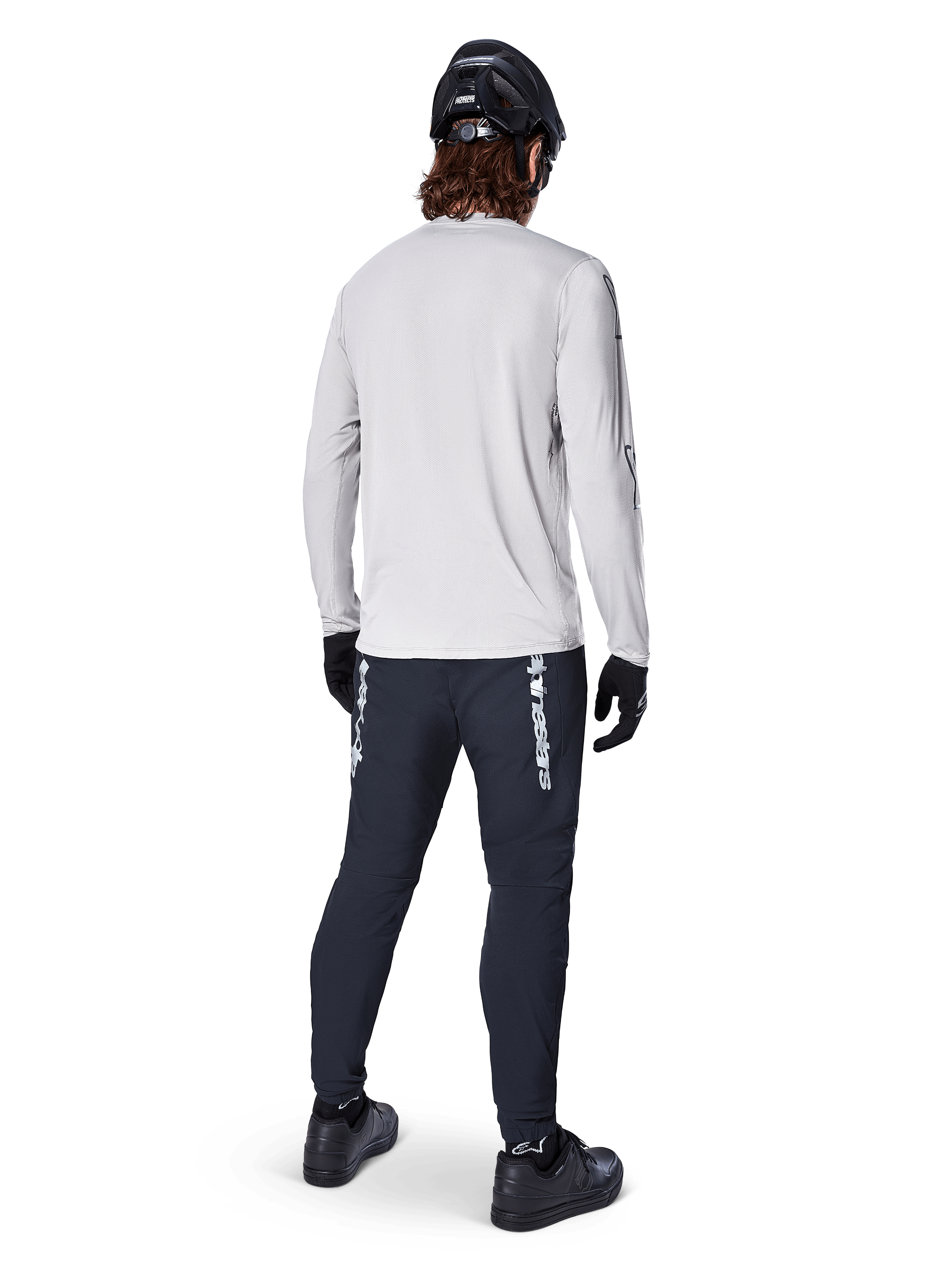 Maglia a maniche lunghe Alpinestars A-Dura Switch, Grigio Chiaro, vista posteriore su un ciclista che indossa pantaloni da ciclismo neri, casco e guanti, abbigliamento da mountain bike ad alte prestazioni con coda posteriore più lunga.