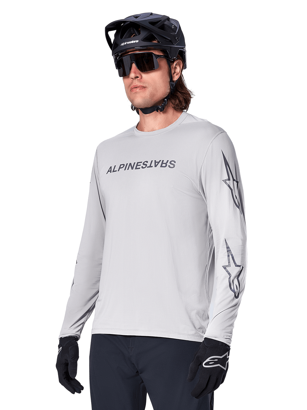 Alpinestars A-Dura Switch Long Sleeve Jersey, maglia da mountain bike, grigio chiaro, logo testuale nero serigrafato sul petto e loghi a stella sulle maniche, indossata con casco da mountain bike nero, occhiali da sole scuri e guanti neri, abbigliamento sportivo per ciclismo fuoristrada