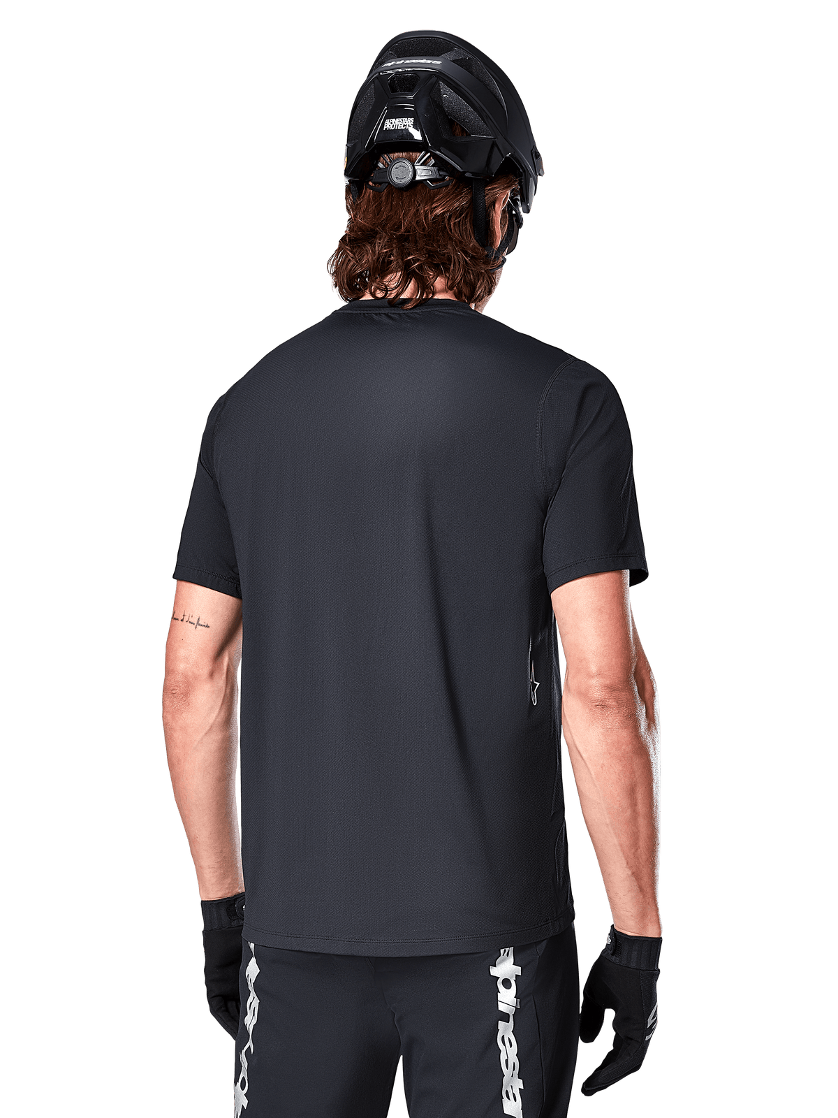 Alpinestars A-Dura Switch Short Sleeve Jersey, nero, vista posteriore su un modello con casco da ciclismo nero e pantaloncini da MTB, mette in risalto la vestibilità regolare e la coda più lunga specifica per la mountain bike