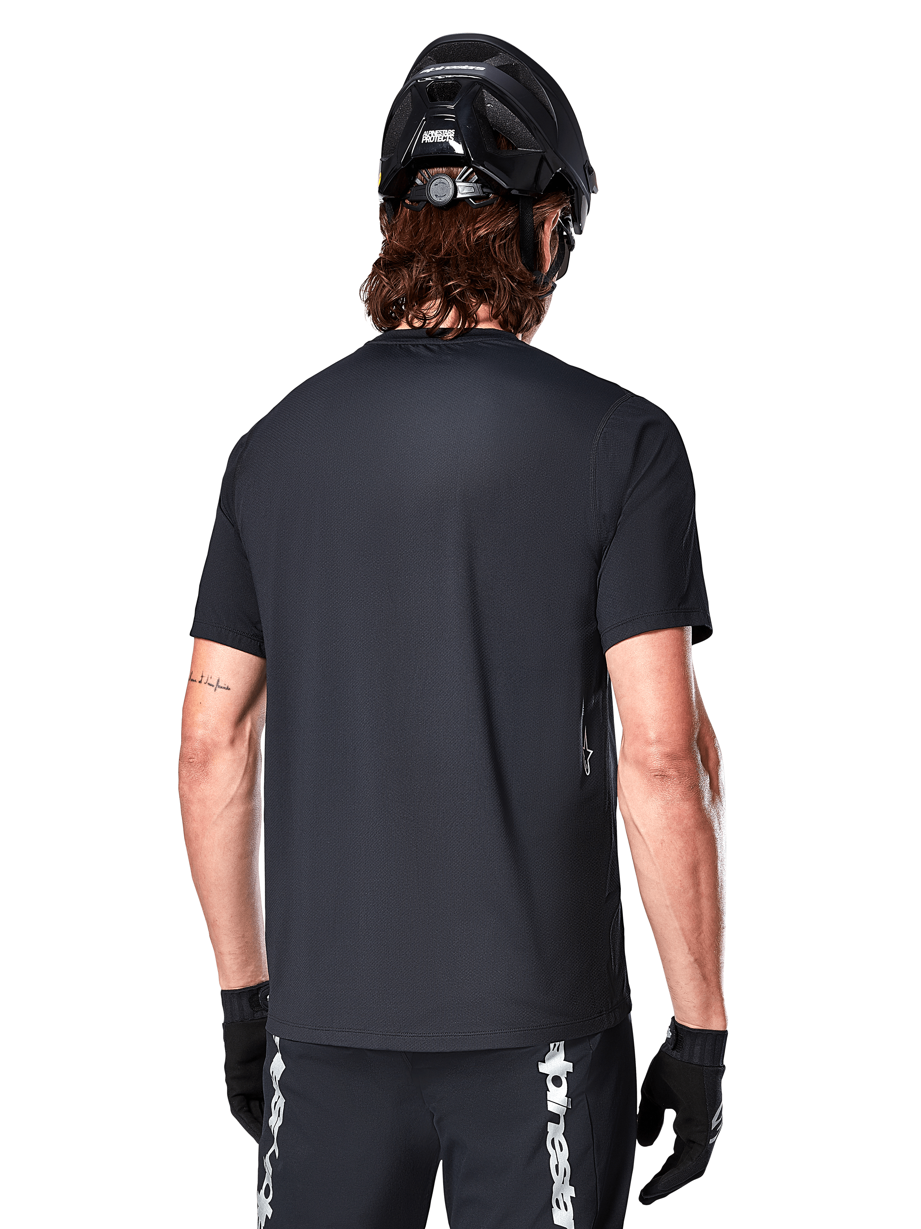 Alpinestars A-Dura Switch Short Sleeve Jersey, nero, vista posteriore su un modello con casco da ciclismo nero e pantaloncini da MTB, mette in risalto la vestibilità regolare e la coda più lunga specifica per la mountain bike