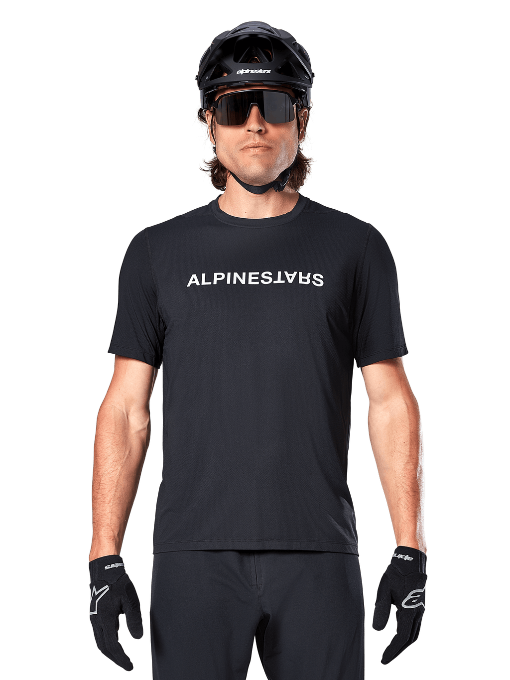 Ciclista di mountain bike con maglia a maniche corte Alpinestars A-Dura Switch in nero, con logo wordmark bianco sul petto, abbinata a casco nero, grandi occhiali da sole e guanti neri, abbigliamento tecnico da ciclismo per trail riding.