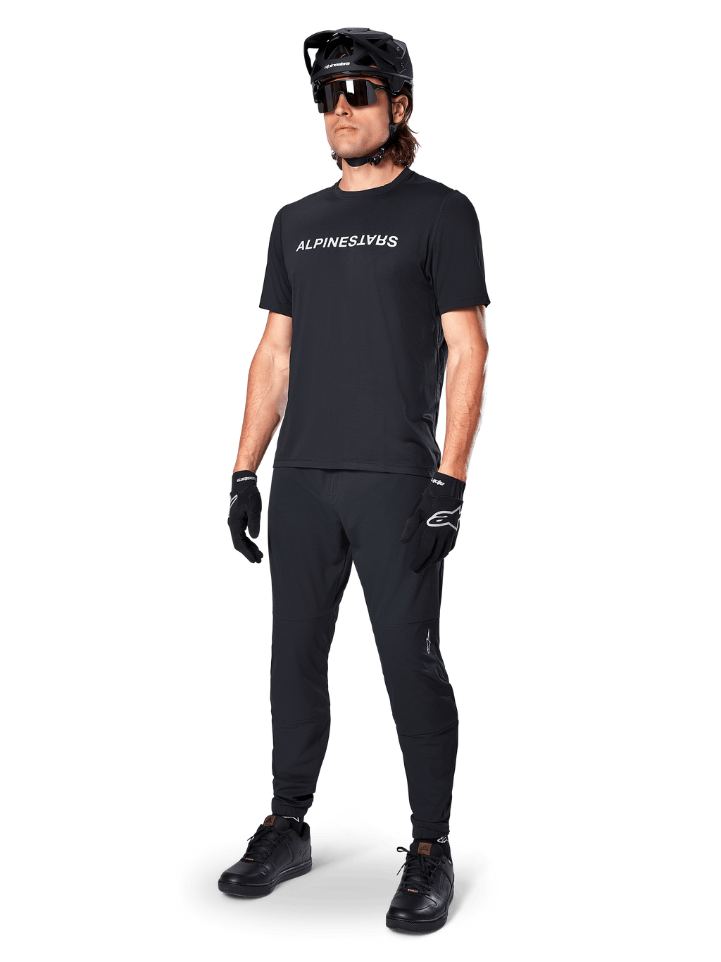Alpinestars A-Dura Switch Short Sleeve Jersey, nero, indossata da un modello con pantaloni da MTB neri coordinati, casco e guanti, con marchio Alpinestars bianco sul petto, abbigliamento tecnico per mountain bike