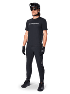 Alpinestars A-Dura Switch Short Sleeve Jersey, nero, indossata da un modello con pantaloni da MTB neri coordinati, casco e guanti, con marchio Alpinestars bianco sul petto, abbigliamento tecnico per mountain bike