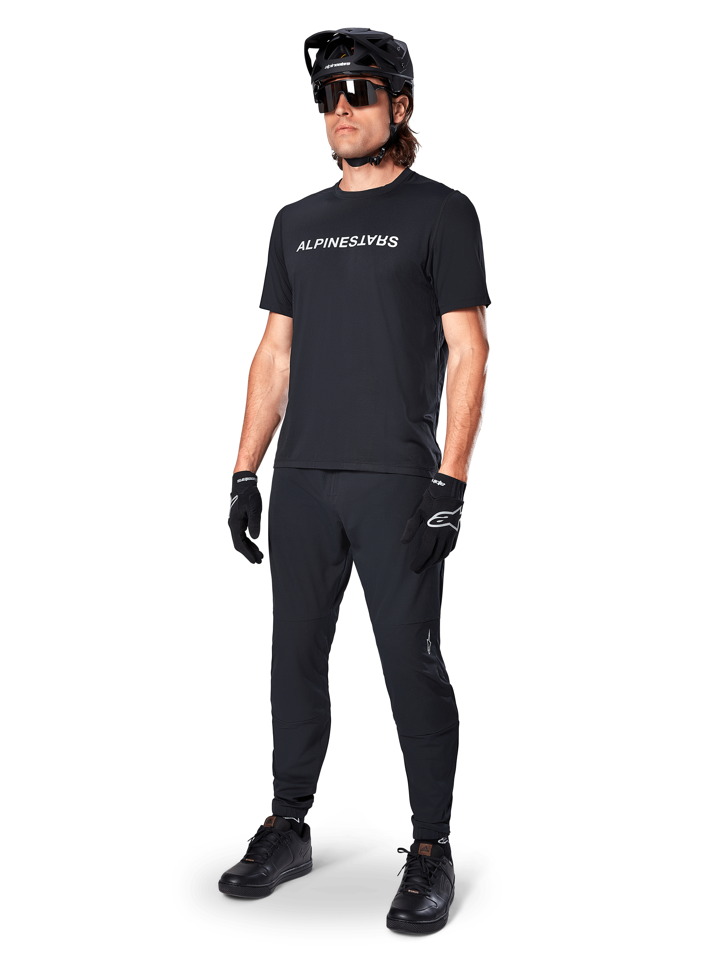 Alpinestars A-Dura Switch Short Sleeve Jersey, nero, indossata da un modello con pantaloni da MTB neri coordinati, casco e guanti, con marchio Alpinestars bianco sul petto, abbigliamento tecnico per mountain bike