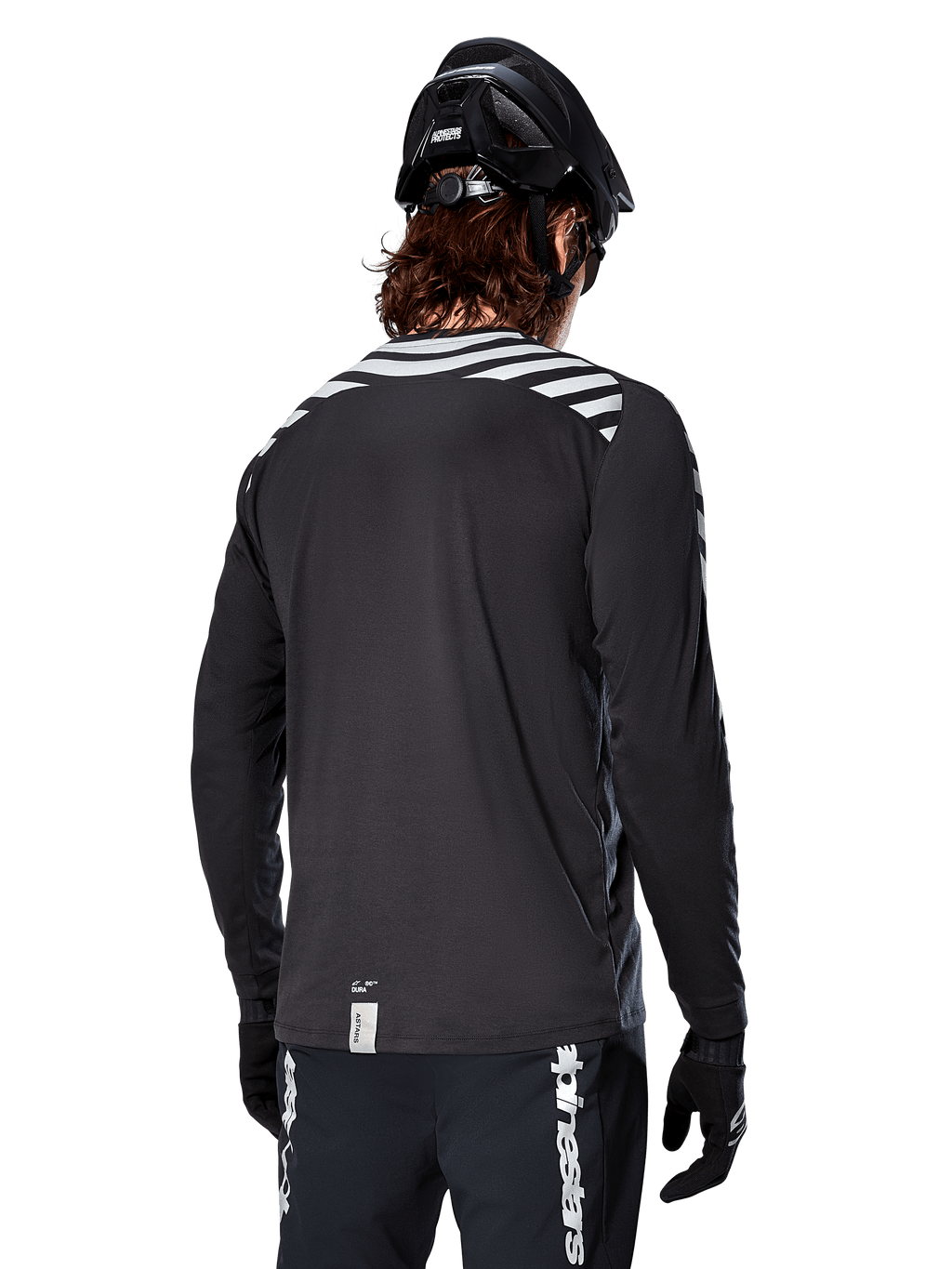 Maglia a maniche lunghe Alpinestars A-Dura Dri Oscar, Nero Riflettente, vista posteriore con strisce diagonali riflettenti sulle spalle e una coda più lunga, indossata con casco e guanti da MTB neri, equipaggiamento tecnico per mountain bike