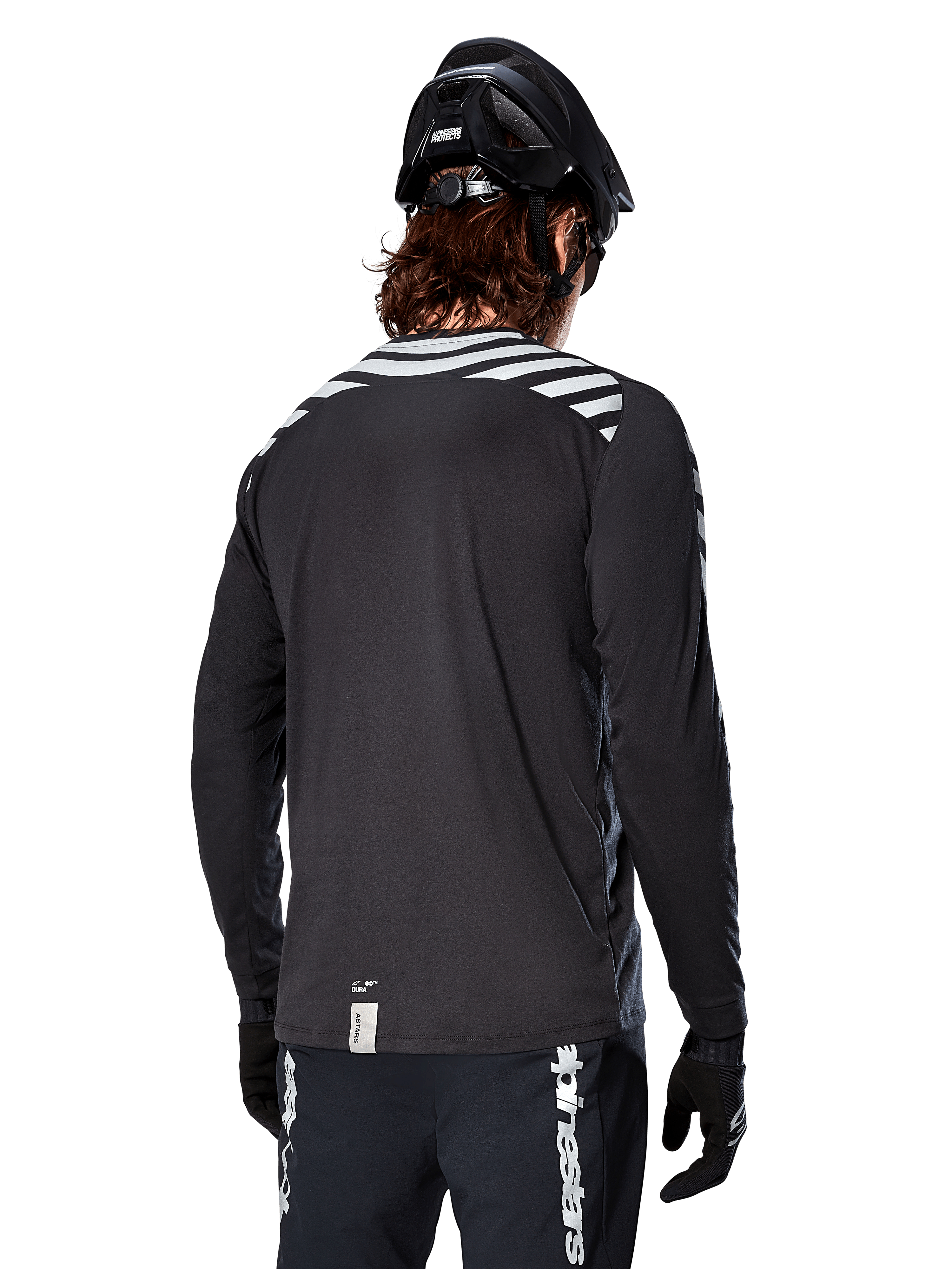 Maglia a maniche lunghe Alpinestars A-Dura Dri Oscar, Nero Riflettente, vista posteriore con strisce diagonali riflettenti sulle spalle e una coda più lunga, indossata con casco e guanti da MTB neri, equipaggiamento tecnico per mountain bike