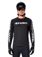 Ciclista uomo che indossa la maglia a maniche lunghe Alpinestars A-Dura Dri Oscar, Black Reflective, con logo Alpinestars bianco sul petto e grafiche riflettenti argento sulle maniche, abbinata a casco da MTB nero, occhiali da sole e guanti neri, abbigliamento tecnico da ciclismo