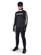 Maglia Alpinestars A-Dura Dri Oscar a maniche lunghe, Nero Riflettente, con scritta Alpinestars bianca sul petto e motivi grafici riflettenti sulle maniche, indossata con pantaloni da mountain bike neri, casco e guanti, abbigliamento tecnico da MTB