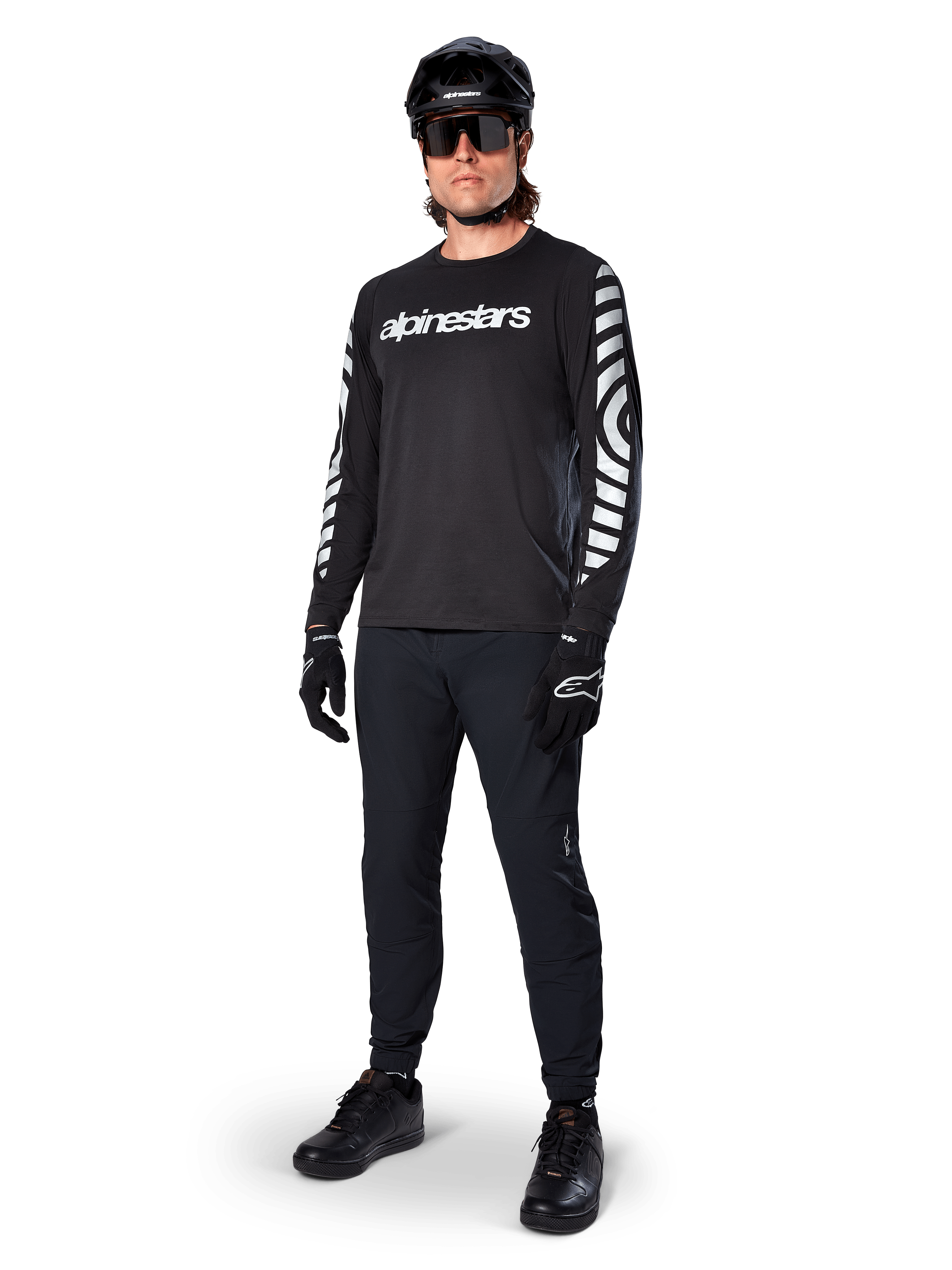Maglia Alpinestars A-Dura Dri Oscar a maniche lunghe, Nero Riflettente, con scritta Alpinestars bianca sul petto e motivi grafici riflettenti sulle maniche, indossata con pantaloni da mountain bike neri, casco e guanti, abbigliamento tecnico da MTB