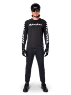 Maglia a maniche lunghe Alpinestars A-Dura Dri Oscar in nero riflettente, indossata con casco nero e occhiali da sole, con logo bianco sul petto e motivi grafici riflettenti sulle maniche, abbigliamento da MTB per guida off-road