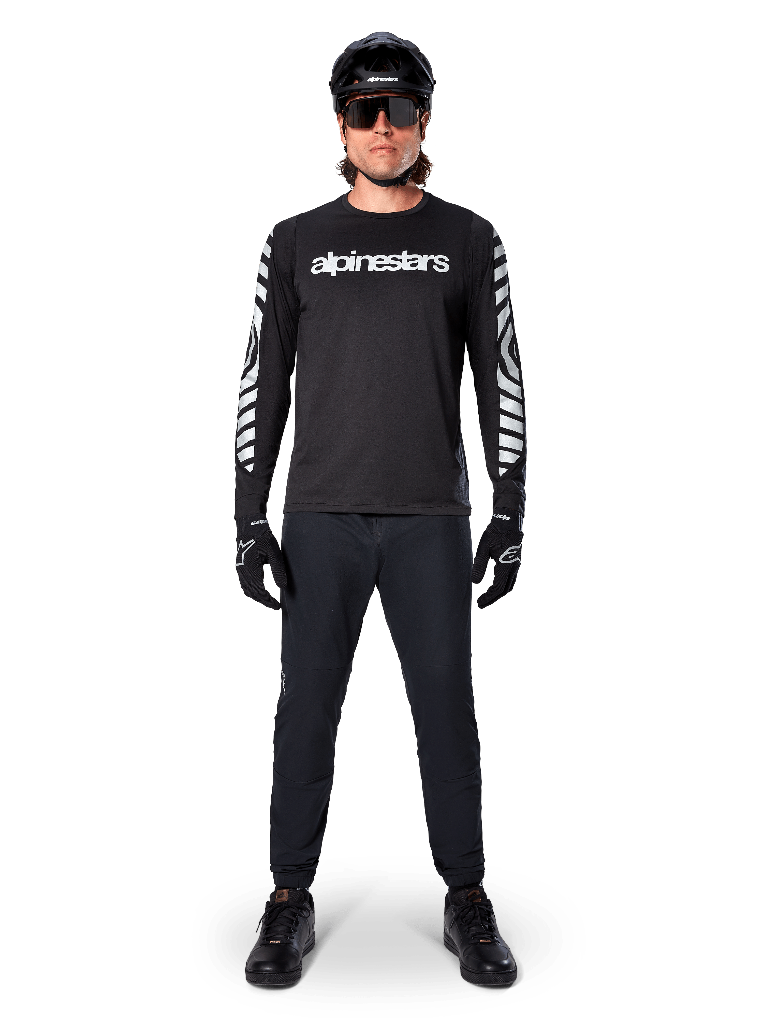 Maglia a maniche lunghe Alpinestars A-Dura Dri Oscar in nero riflettente, indossata con casco nero e occhiali da sole, con logo bianco sul petto e motivi grafici riflettenti sulle maniche, abbigliamento da MTB per guida off-road