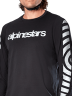 Maglia a maniche lunghe Alpinestars A-Dura Dri Oscar, Black Reflective, vista ravvicinata che mostra il logo Alpinestars bianco sul petto e grafiche circolari riflettenti sulle maniche, abbigliamento tecnico da ciclismo per mountain bike
