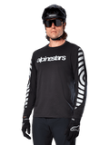 Alpinestars A-Dura Dri Oscar Jersey a maniche lunghe, maglia da ciclismo MTB, nero riflettente, con logo bianco sul petto e grafiche circolari riflettenti sulle maniche, indossata con casco nero e occhiali da sole, abbigliamento tecnico traspirante per mountain bike