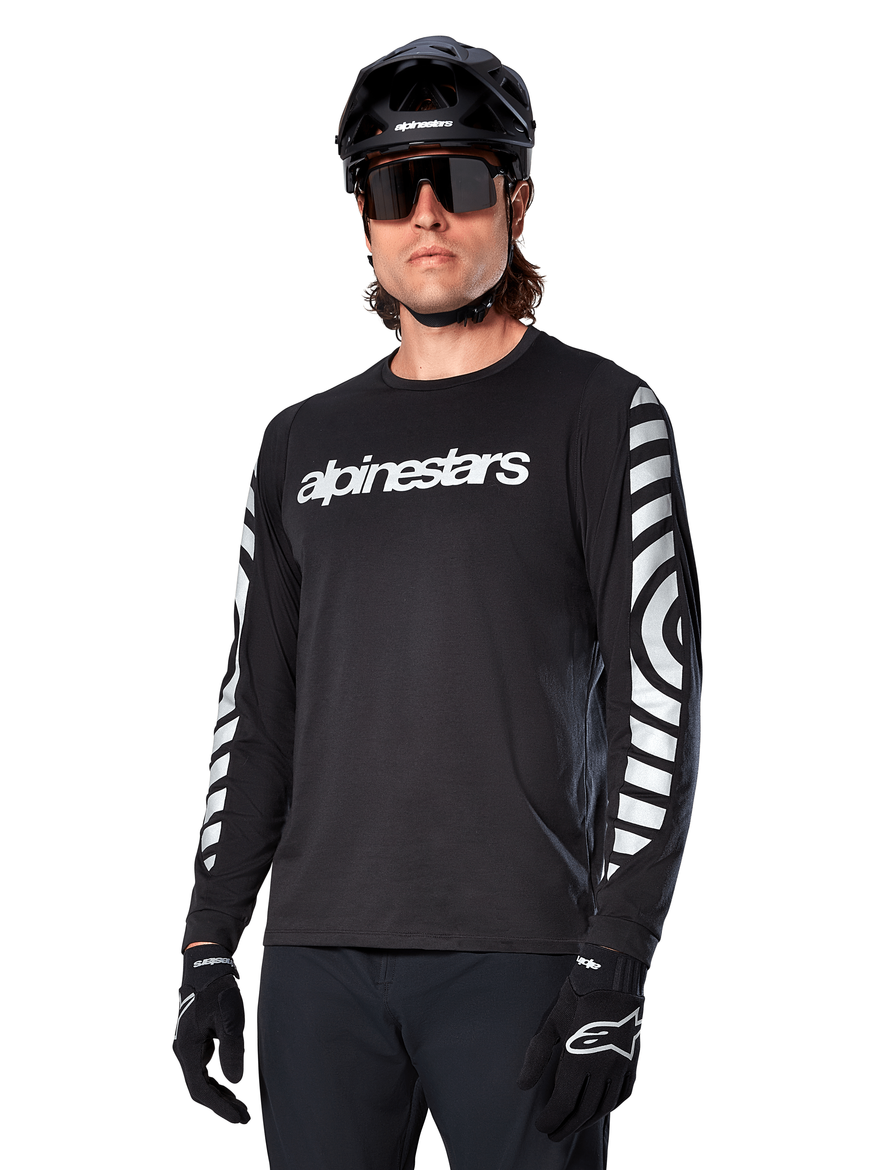 Alpinestars A-Dura Dri Oscar Jersey a maniche lunghe, maglia da ciclismo MTB, nero riflettente, con logo bianco sul petto e grafiche circolari riflettenti sulle maniche, indossata con casco nero e occhiali da sole, abbigliamento tecnico traspirante per mountain bike