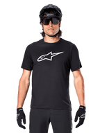 Maglia Alpinestars A-Dura Dri Oscar a maniche corte, nero riflettente, indossata con casco MTB nero, occhiali da sole e guanti, con un evidente logo bianco sul petto, abbigliamento tecnico per mountain bike