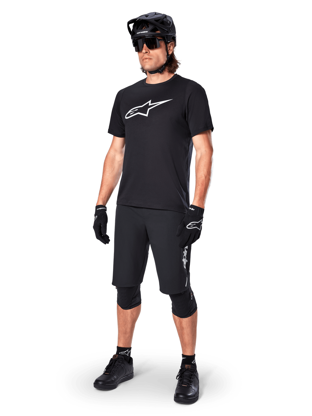 Ciclista di mountain bike che indossa la maglia a maniche corte Alpinestars A-Dura Dri Oscar in Black Reflective, con un grande logo bianco sul petto, abbinata a pantaloncini MTB, guanti e casco neri coordinati, abbigliamento tecnico da ciclismo per prestazioni fuoristrada