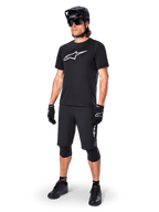 Ciclista di mountain bike che indossa la maglia a maniche corte Alpinestars A-Dura Dri Oscar in Black Reflective, con un grande logo bianco sul petto, abbinata a pantaloncini MTB, guanti e casco neri coordinati, abbigliamento tecnico da ciclismo per prestazioni fuoristrada