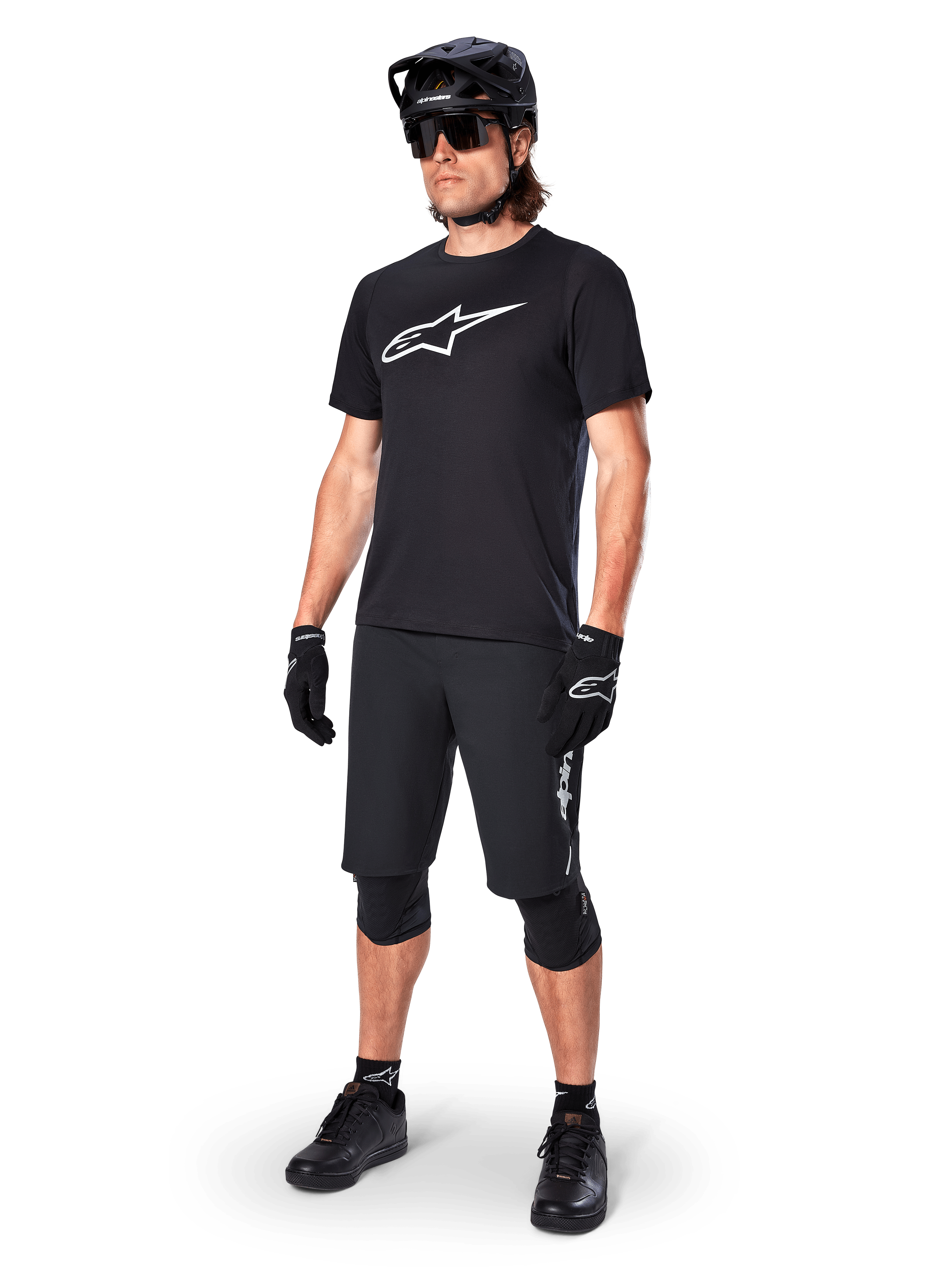 Ciclista di mountain bike che indossa la maglia a maniche corte Alpinestars A-Dura Dri Oscar in Black Reflective, con un grande logo bianco sul petto, abbinata a pantaloncini MTB, guanti e casco neri coordinati, abbigliamento tecnico da ciclismo per prestazioni fuoristrada