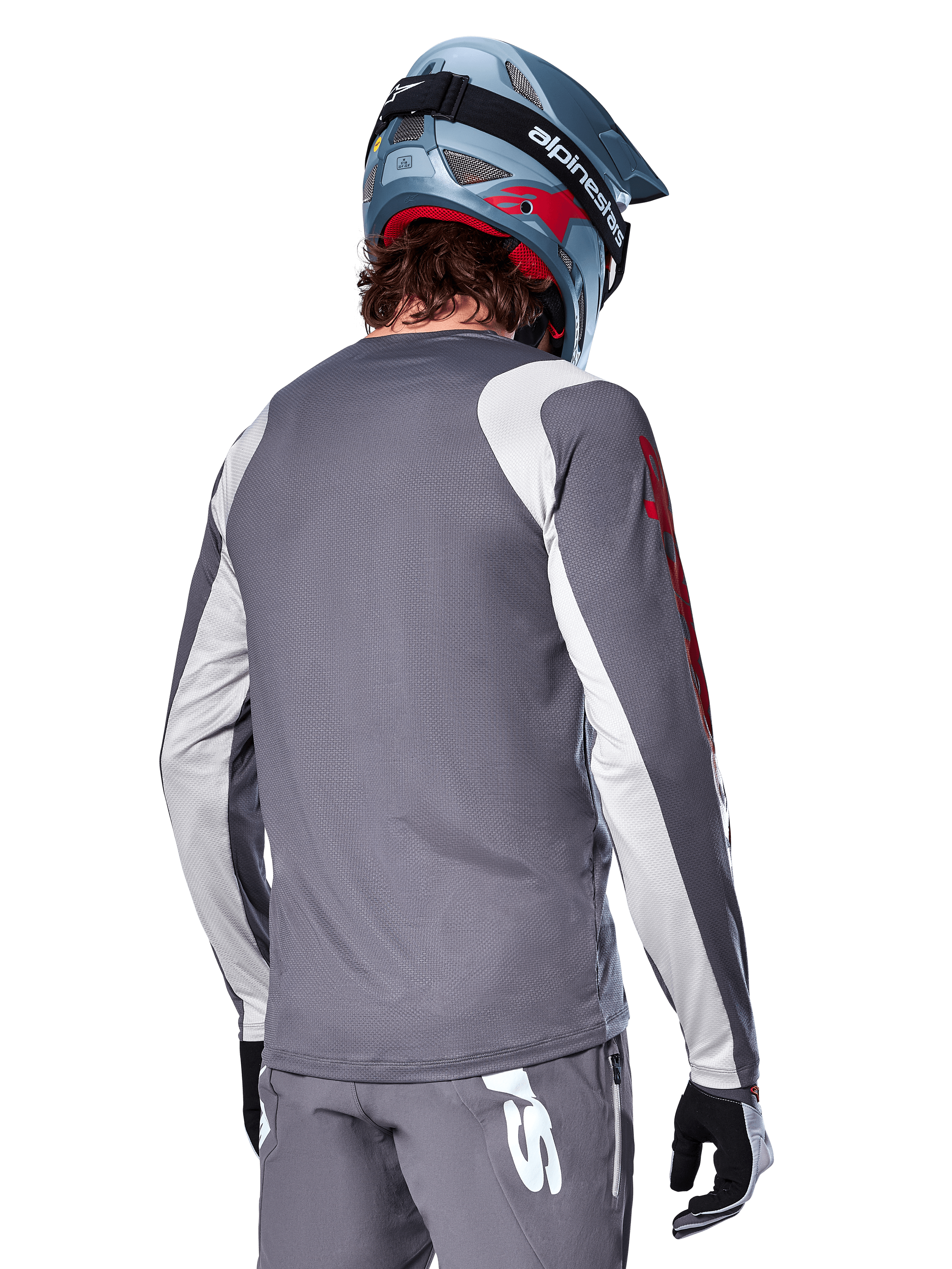 Alpinestars Maglia a maniche lunghe A-Supra Astar, grigio scuro con pannelli grigio chiaro su spalle e braccia, vista posteriore di un pilota con casco integrale da mountain bike blu e pantaloni grigi, abbigliamento da ciclismo MTB con vestibilità performante