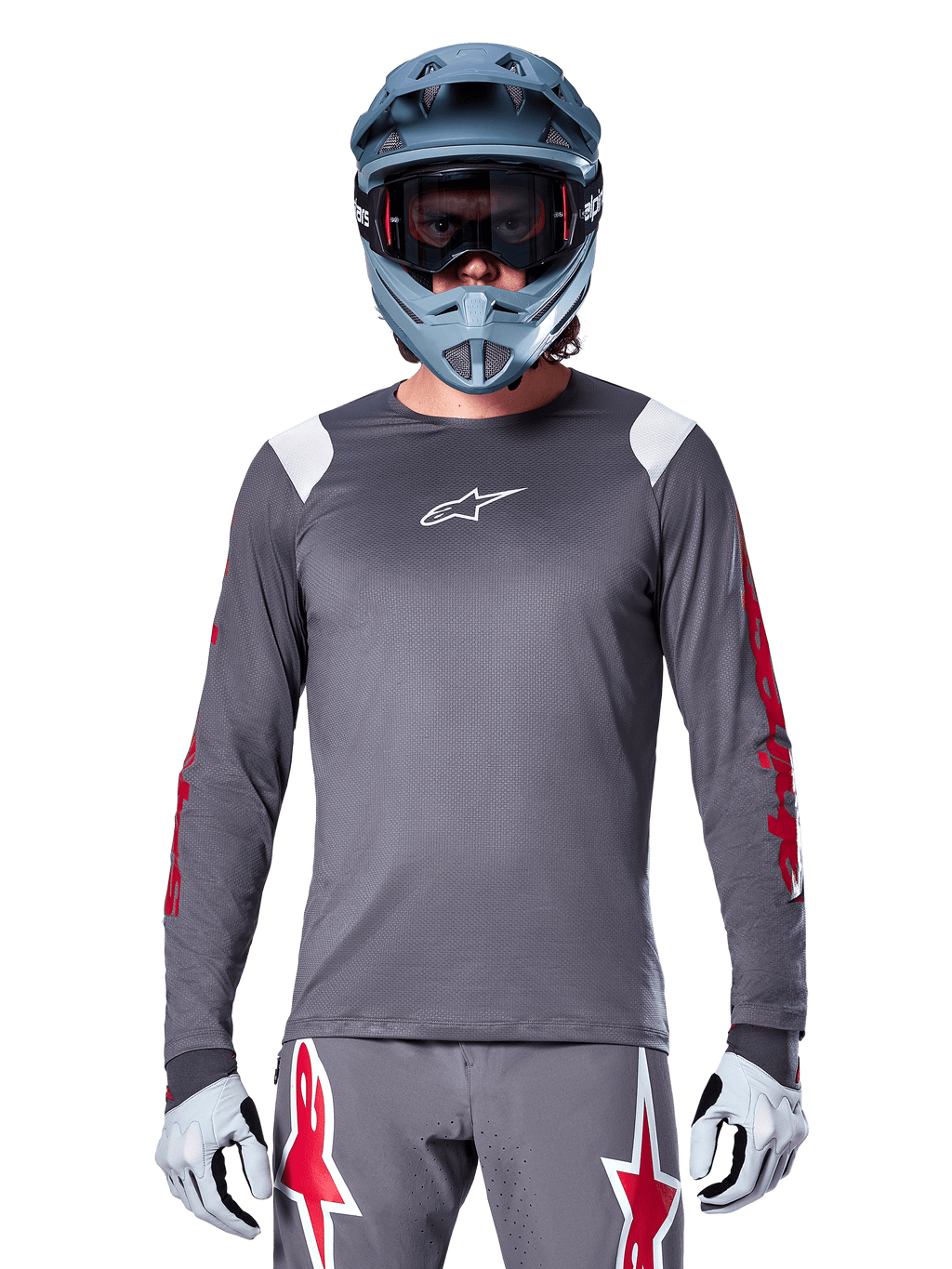 Ciclista MTB con maglia a maniche lunghe Alpinestars A-Supra Astar, grigio scuro con grafiche rosse sulle maniche e dettagli bianchi sulle spalle, pantaloni grigi coordinati con loghi a stella rossi, casco integrale blu e maschera, equipaggiamento da ciclismo fuoristrada coordinato