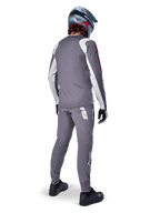 Alpinestars A-Supra Astar Jersey, maglia da MTB a maniche lunghe, grigio scuro con dettagli bianchi sulle maniche e logo rosso, vista posteriore del rider con pantaloni grigi abbinati e casco integrale blu, abbigliamento tecnico da ciclismo