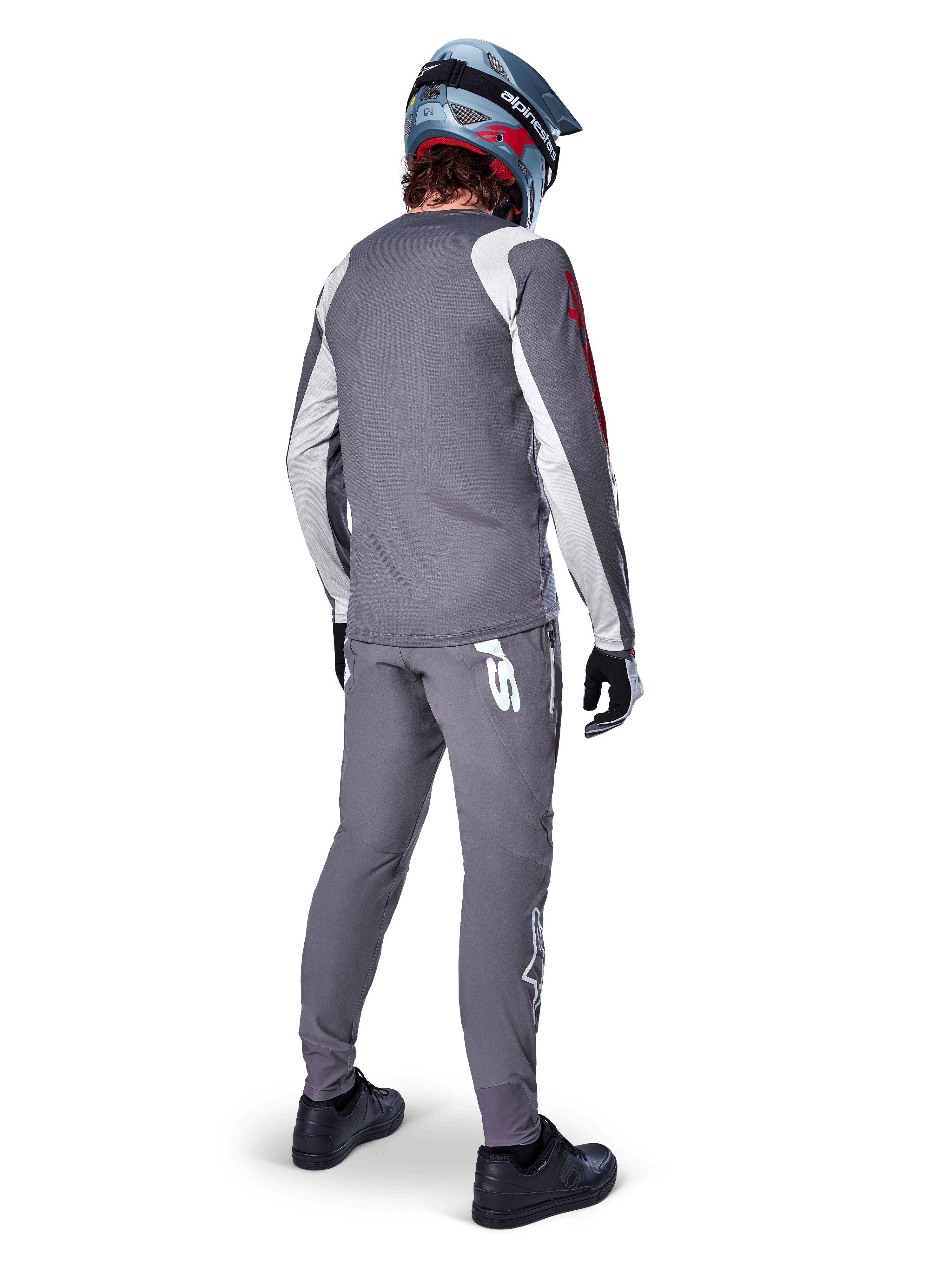 Alpinestars A-Supra Astar Jersey, maglia da MTB a maniche lunghe, grigio scuro con dettagli bianchi sulle maniche e logo rosso, vista posteriore del rider con pantaloni grigi abbinati e casco integrale blu, abbigliamento tecnico da ciclismo