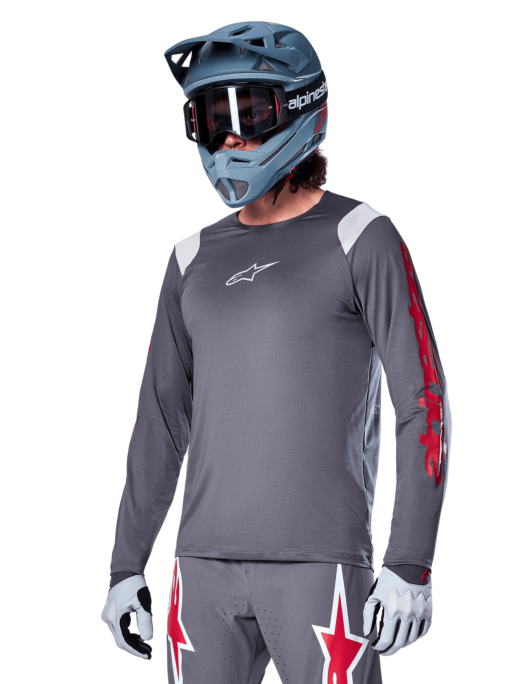 Alpinestars A-Supra Astar Jersey a maniche lunghe, maglia da mountain bike MTB, grigio scuro con accenti rossi e bianchi, vestibilità performance, indossata con pantaloni grigi coordinati con grafiche a stella rosse e bianche, completo da ciclismo off-road con casco integrale e guanti