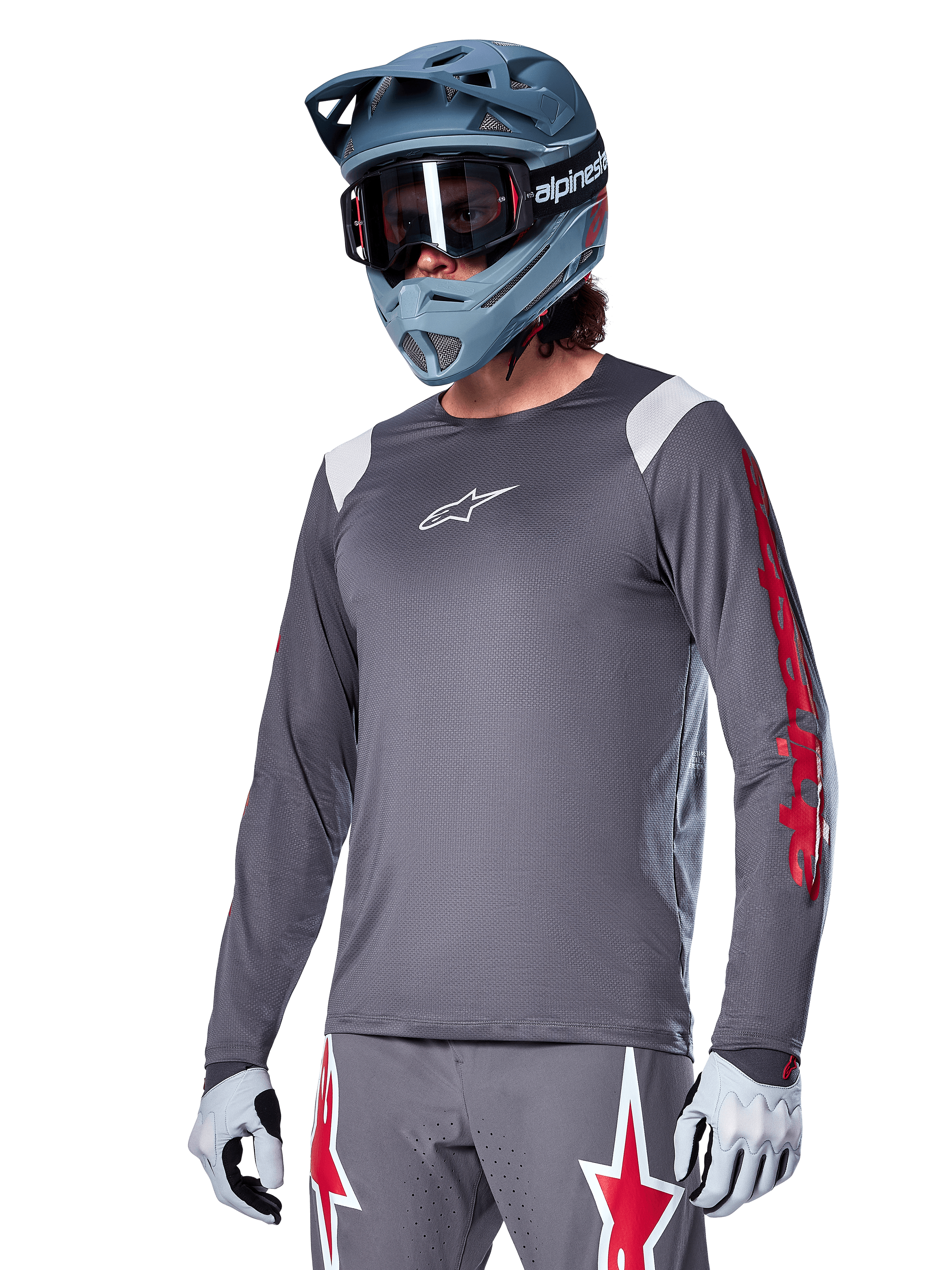 Alpinestars A-Supra Astar Jersey a maniche lunghe, maglia da mountain bike MTB, grigio scuro con accenti rossi e bianchi, vestibilità performance, indossata con pantaloni grigi coordinati con grafiche a stella rosse e bianche, completo da ciclismo off-road con casco integrale e guanti