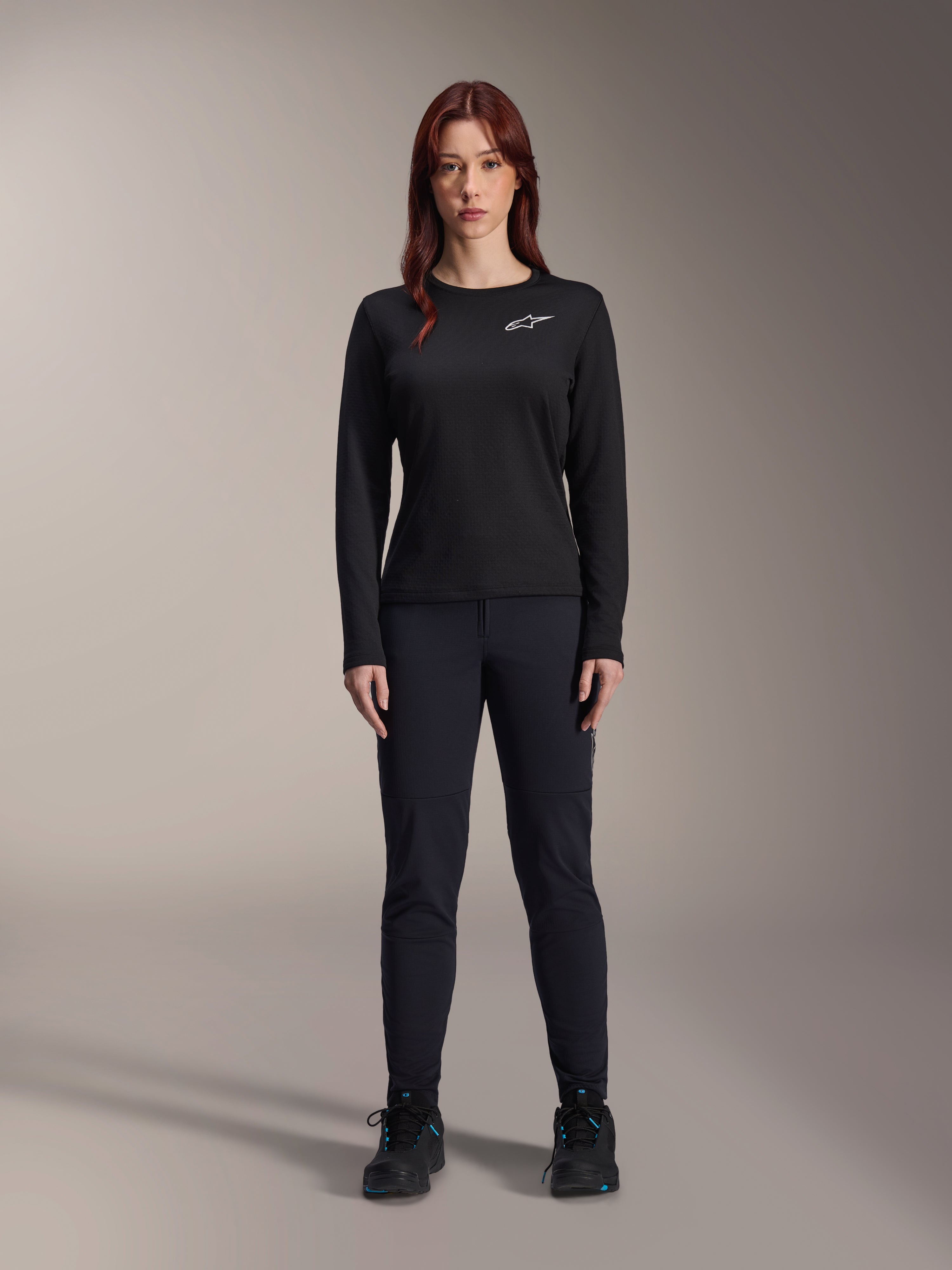 Alpinestars Stella A-Dura Thermal Jersey, maglia da mountain bike a maniche lunghe da donna in nero, con logo bianco sul petto, indossata con abbigliamento nero coordinato e scarpe da ciclismo, ritratto in studio.