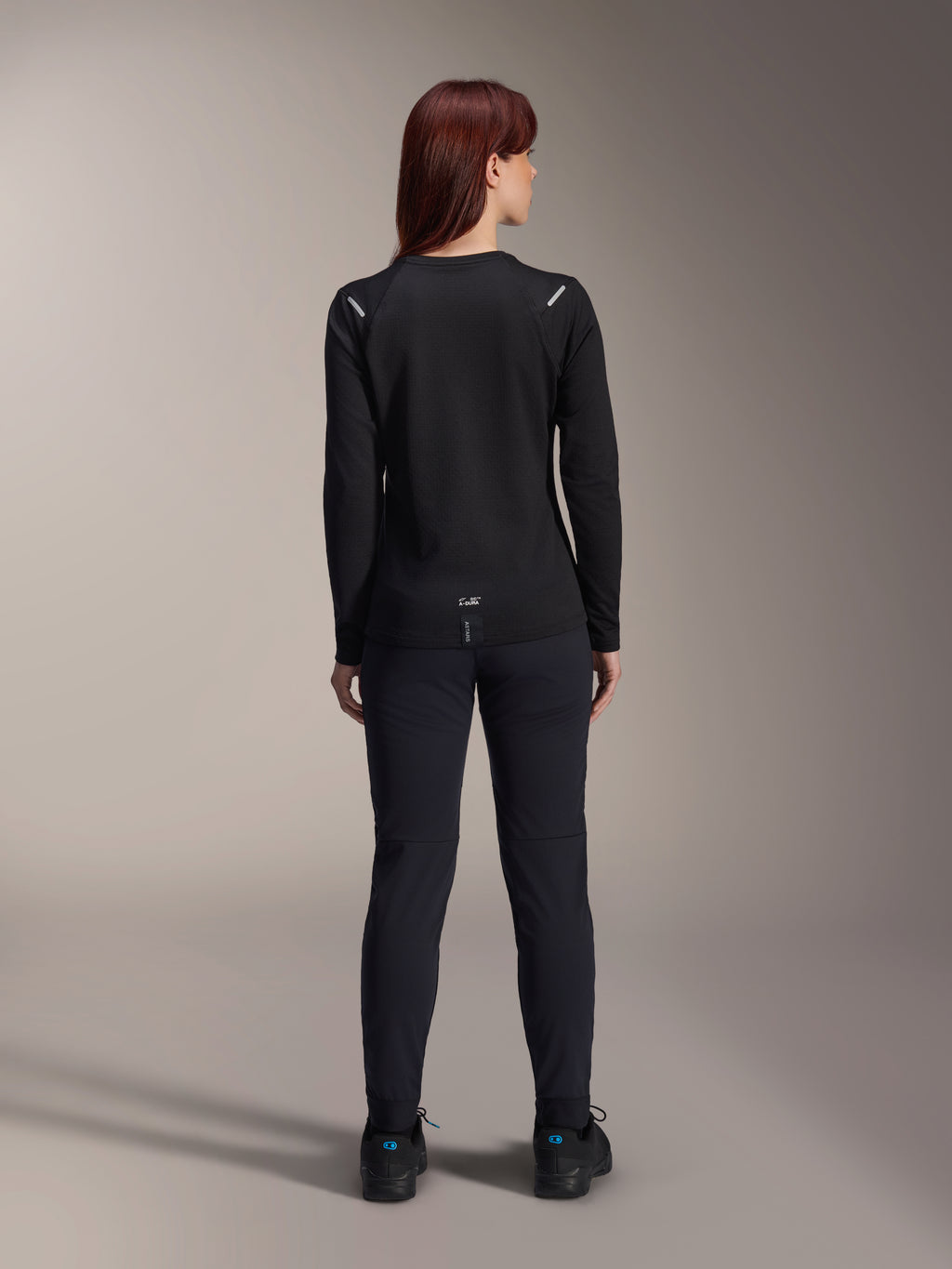 Alpinestars Stella A-Dura Thermal Jersey da donna, vista posteriore, nero, maglia da ciclismo a maniche lunghe con pile isolante, indossata con pantaloni e scarpe neri coordinati, caratterizzata dal piccolo logo A-Dura sulla parte bassa della schiena e dettagli riflettenti sulle spalle, specifica per MTB.
