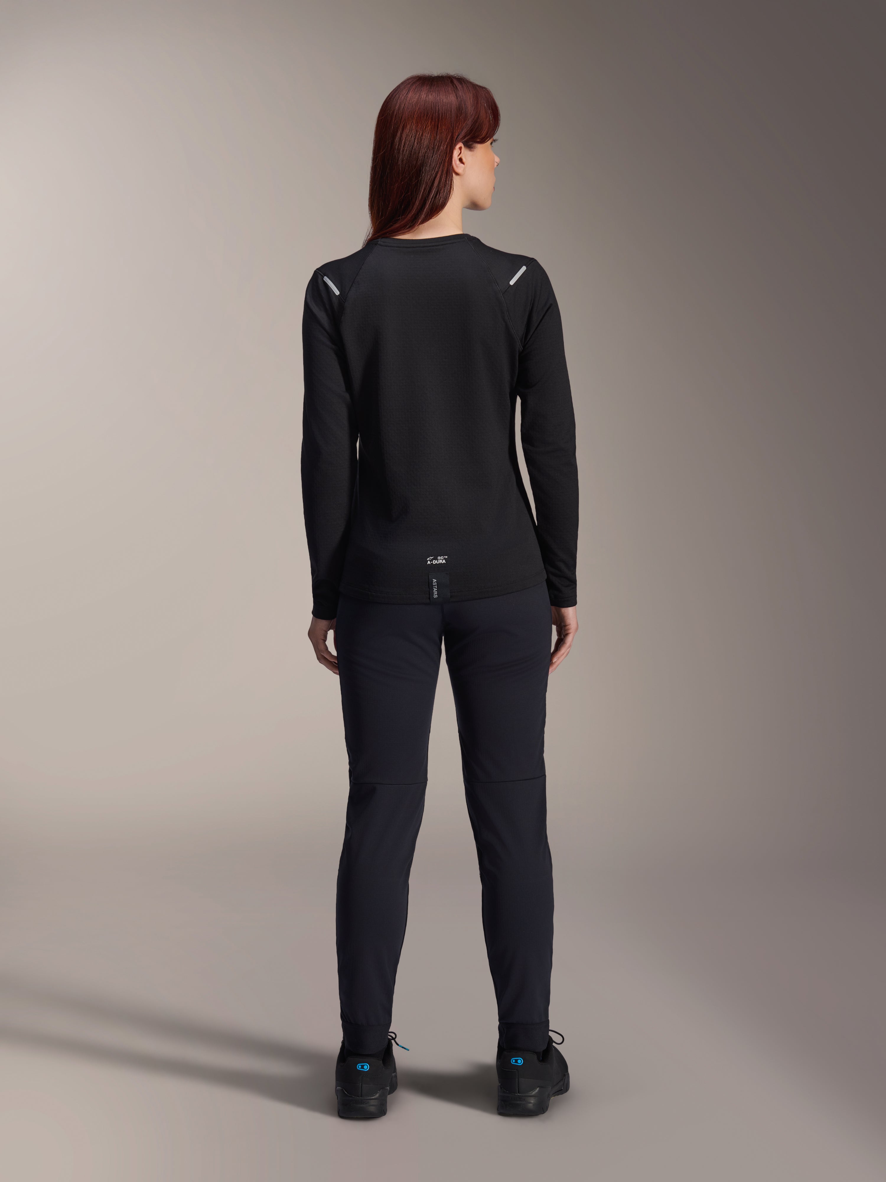 Alpinestars Stella A-Dura Thermal Jersey da donna, vista posteriore, nero, maglia da ciclismo a maniche lunghe con pile isolante, indossata con pantaloni e scarpe neri coordinati, caratterizzata dal piccolo logo A-Dura sulla parte bassa della schiena e dettagli riflettenti sulle spalle, specifica per MTB.