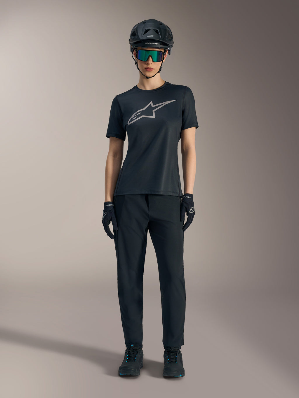Maglia Stella A-Dura Ride SS da donna nera con logo argento, abbinata a pantaloni e casco MTB per guida fuoristrada.