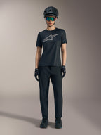 Maglia Stella A-Dura Ride SS da donna nera con logo argento, abbinata a pantaloni e casco MTB per guida fuoristrada.