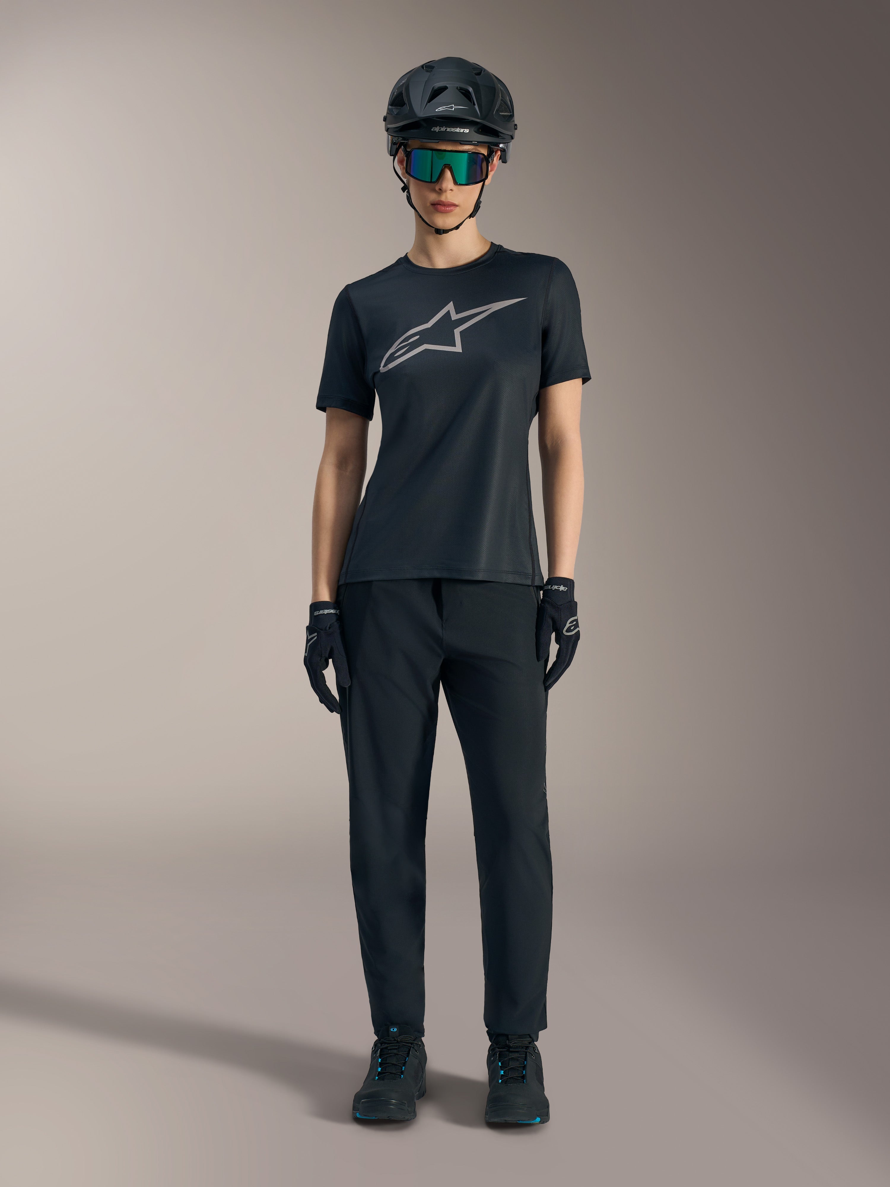 Maglia Stella A-Dura Ride SS da donna nera con logo argento, abbinata a pantaloni e casco MTB per guida fuoristrada.