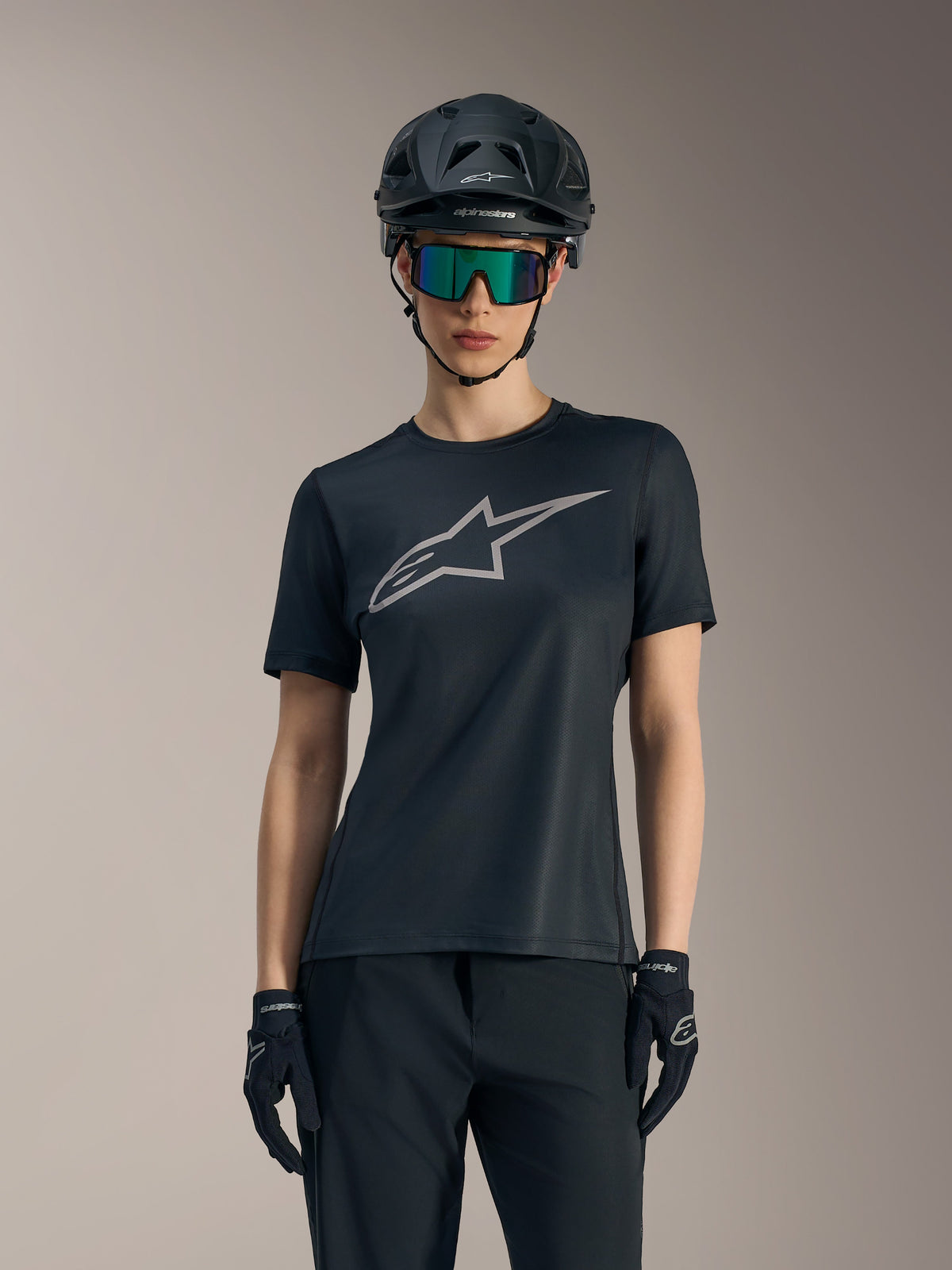 Maglia Stella A-Dura Ride Alpinestars nera da donna con logo grigio, abbinata a casco da mountain bike e occhiali.