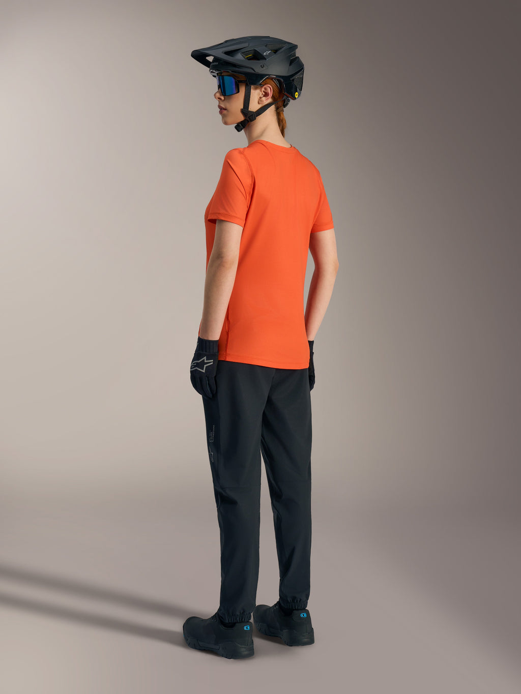 Maglia Alpinestars Stella A-Dura Ride arancione da donna, vista posteriore con pantaloni MTB neri e casco.