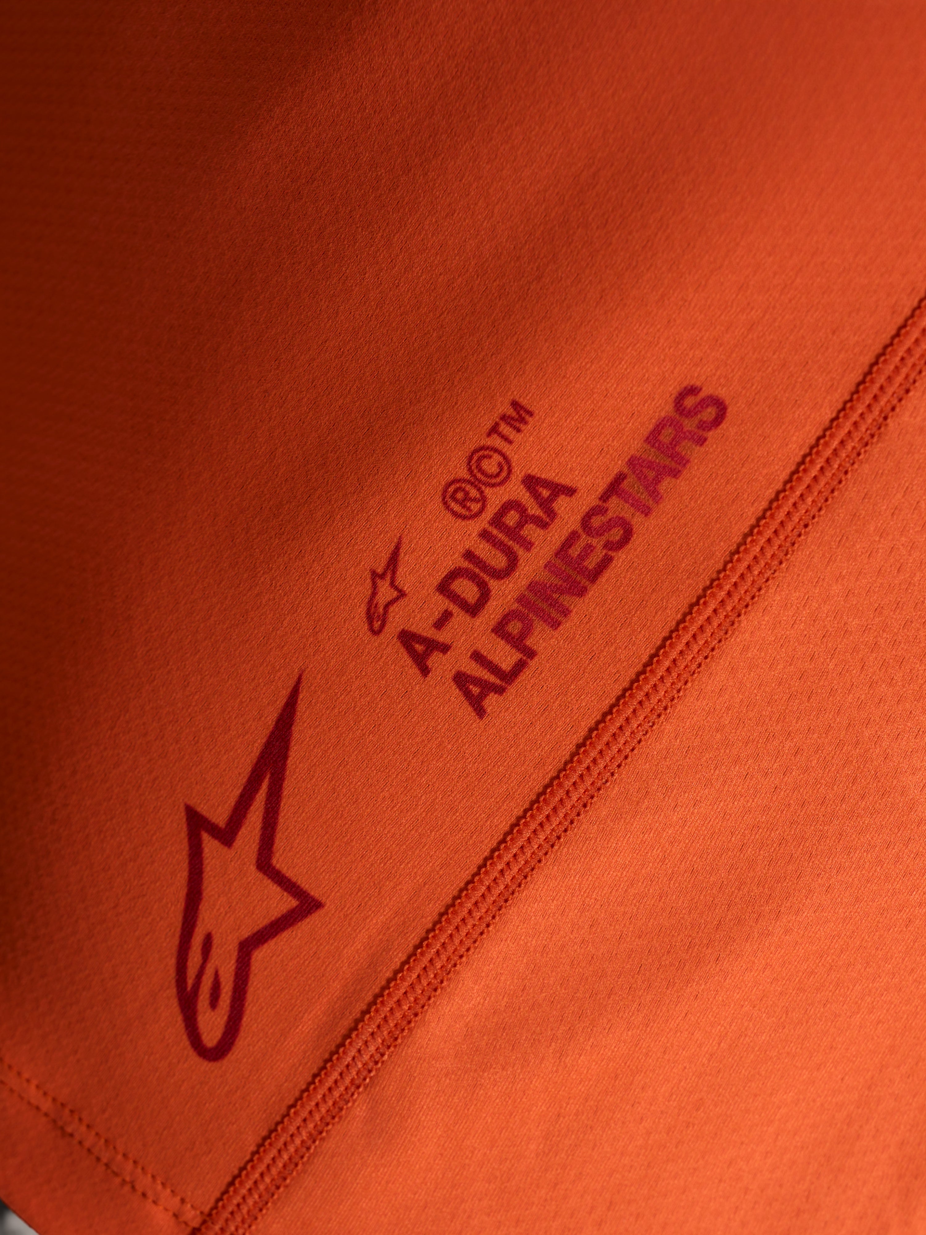 Maglia arancione Stella A-Dura Ride, dettaglio logo Alpinestars e scritta A-DURA su tessuto stretch tecnico.