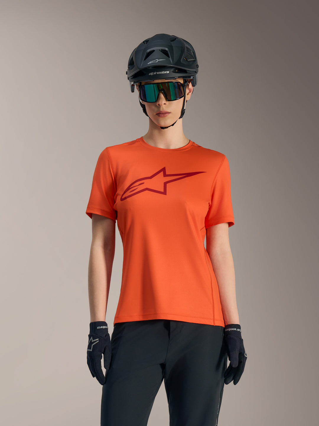 Maglia arancione Stella A-Dura Ride da donna con logo rosso, abbinata a casco MTB nero e occhiali da sole.