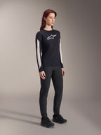Donna che indossa abbigliamento MTB Alpinestars, maglia Stella A-Dura Elite nera con logo bianco sul petto e pannelli sulle maniche, pantaloni Stella A-Dura neri, scarpe da ciclismo nere con accenti blu, outfit completo ad alte prestazioni per mountain bike