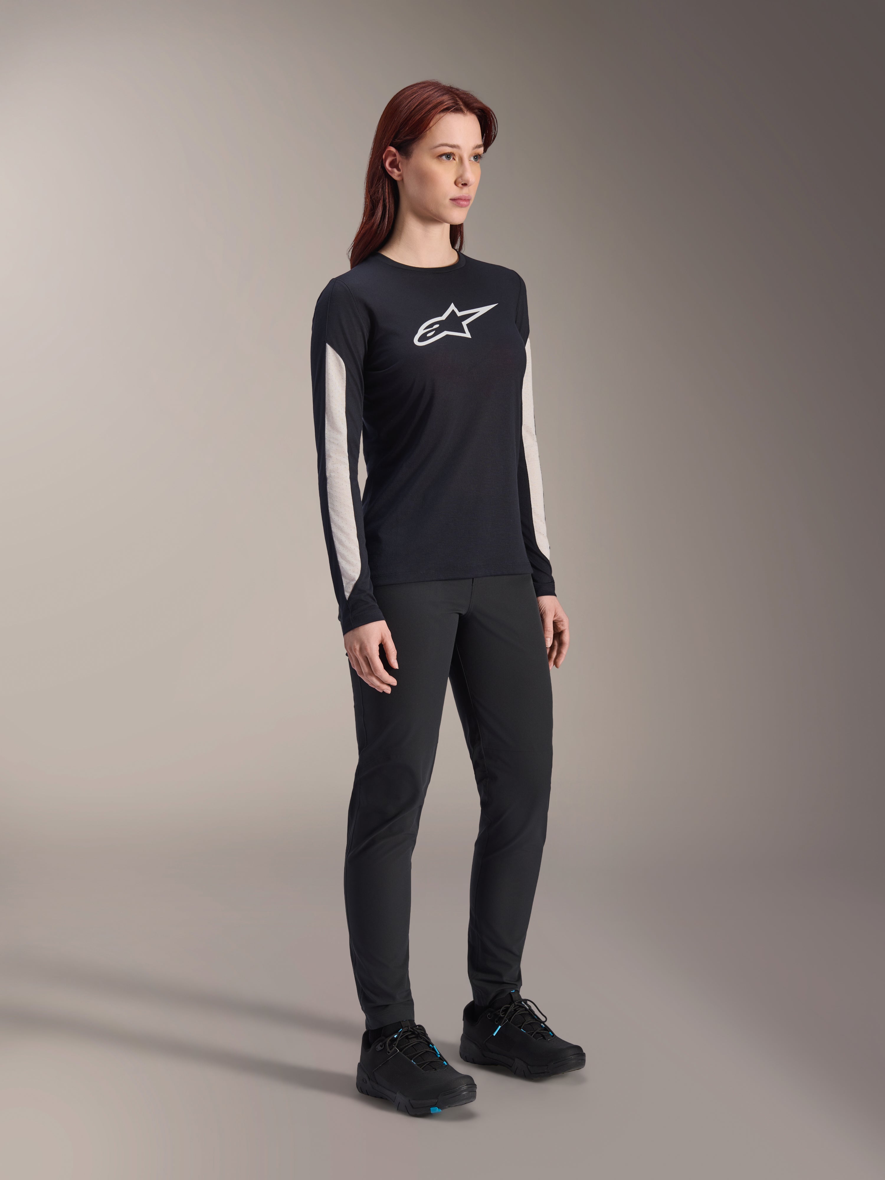 Donna che indossa abbigliamento MTB Alpinestars, maglia Stella A-Dura Elite nera con logo bianco sul petto e pannelli sulle maniche, pantaloni Stella A-Dura neri, scarpe da ciclismo nere con accenti blu, outfit completo ad alte prestazioni per mountain bike
