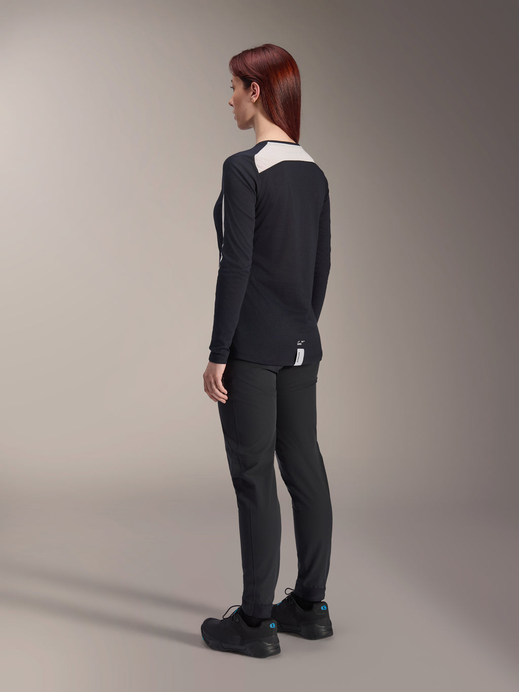 Ciclista con pantaloni Alpinestars Stella A-Dura da donna e maglia Stella A-Dura Elite, nero, vista posteriore con pannelli in rete bianca sulle spalle della maglia a maniche lunghe, pantaloni tecnici slim-fit, abbigliamento coordinato ad alte prestazioni per mountain bike.