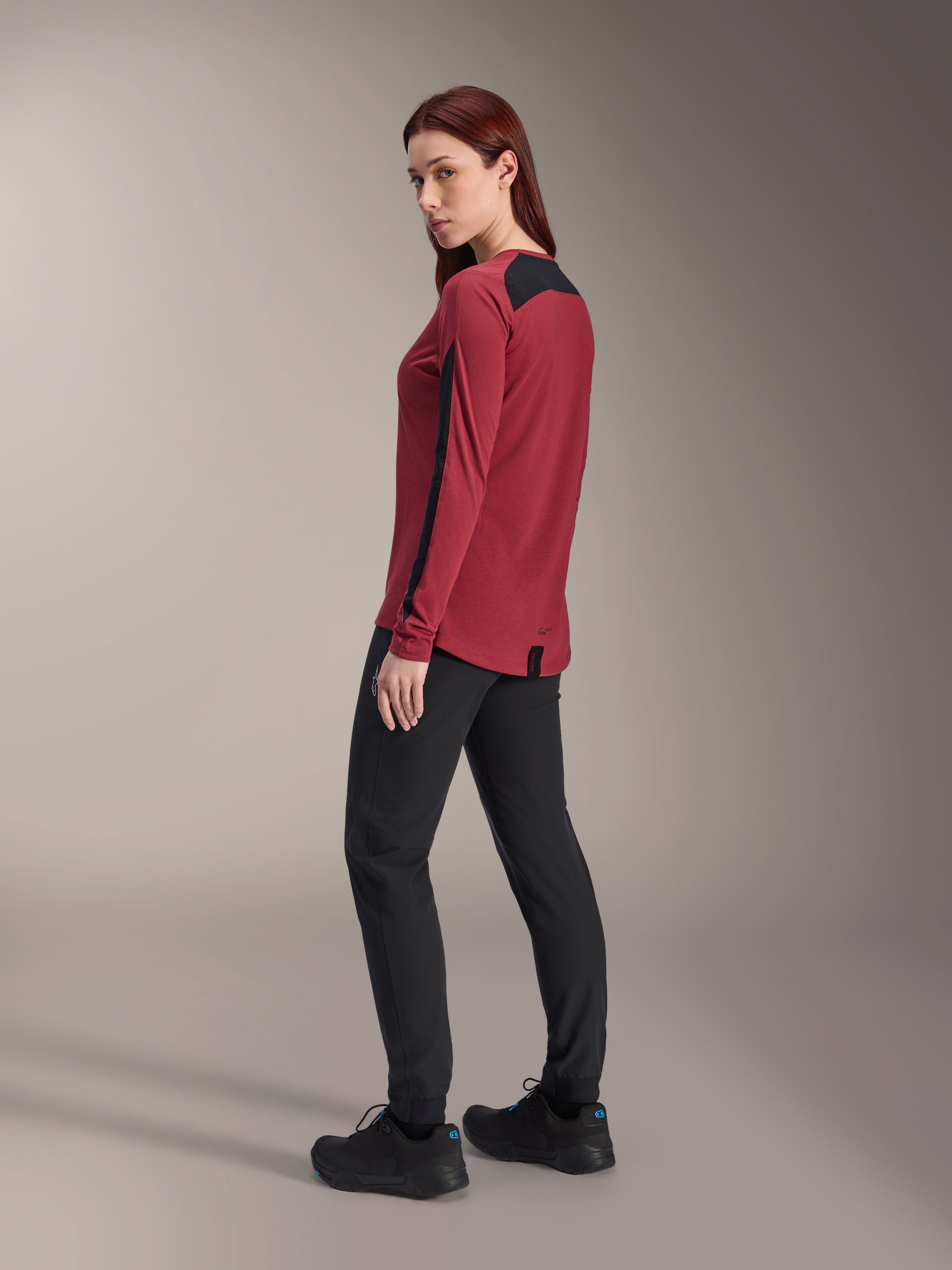 Maglia a maniche lunghe Alpinestars Stella A-Dura Dri Astar Donna, bordeaux e nero, indossata con pantaloni da MTB neri e scarpe nere, vista laterale posteriore, tessuto drirelease riciclato con pannelli in mesh, abbigliamento tecnico da mountain bike