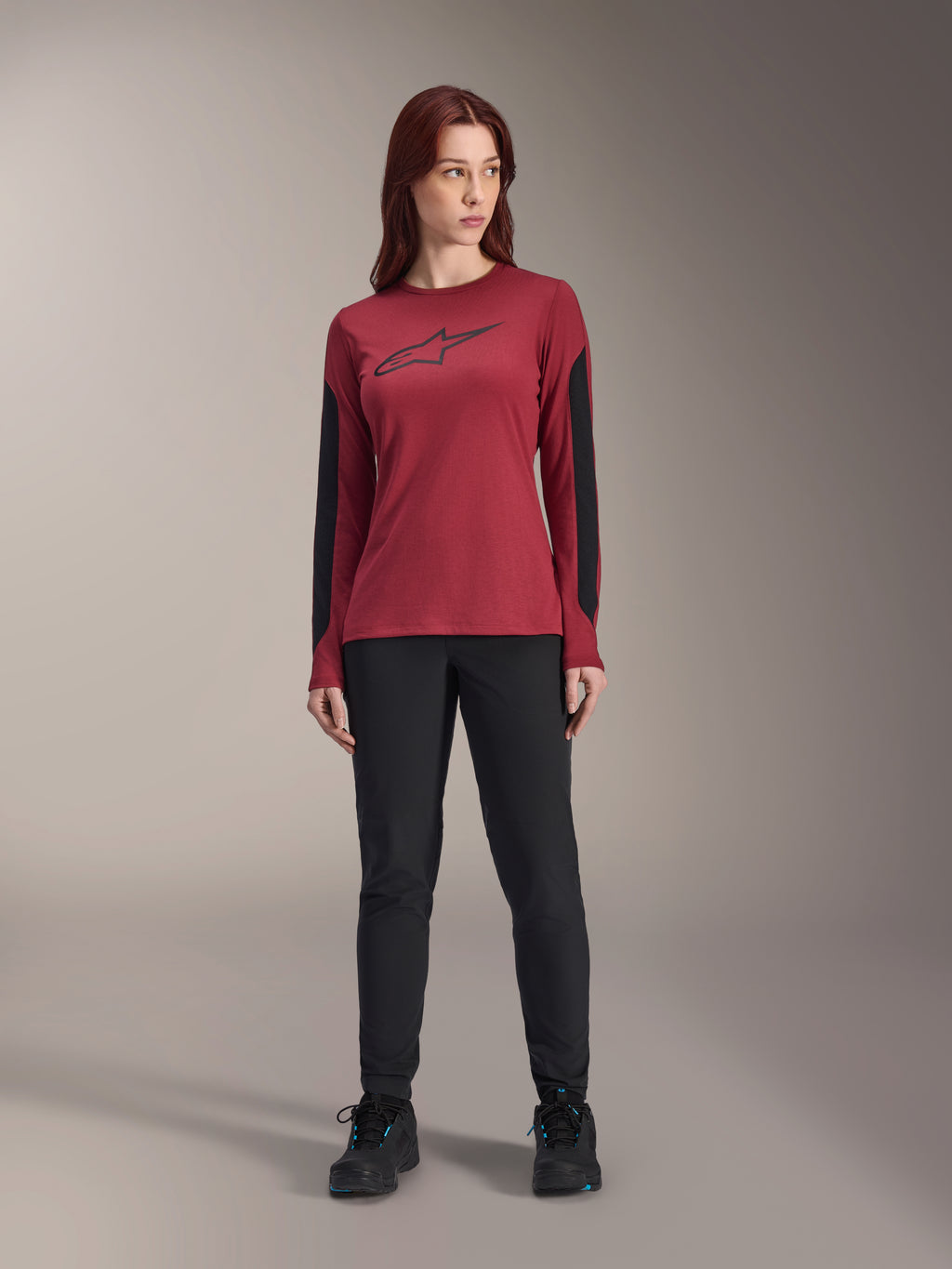 Maglia a maniche lunghe da donna Alpinestars Stella A-Dura Dri Astar in bordeaux, con logo Astars nero sul petto e pannelli in mesh nero sulle braccia, abbinata a pantaloni tecnici neri e scarpe sportive, abbigliamento performance da mountain bike per donna