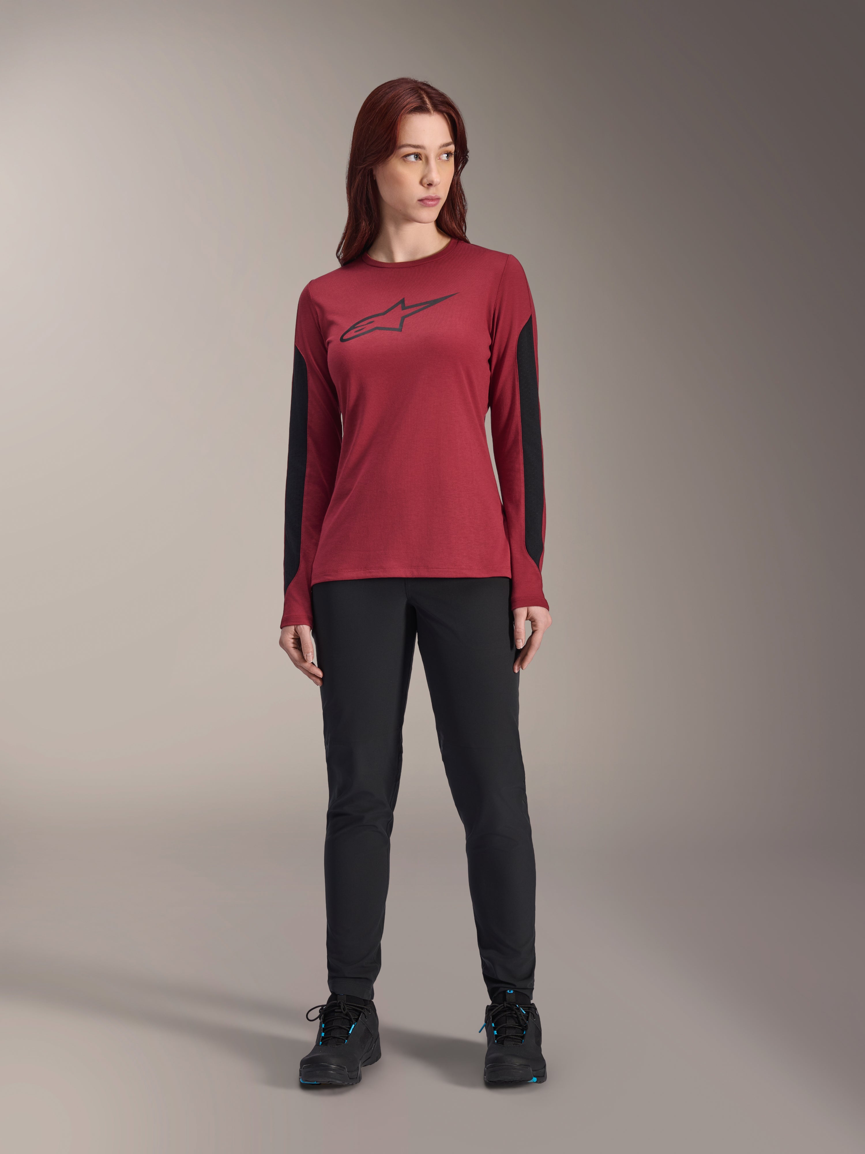 Maglia a maniche lunghe da donna Alpinestars Stella A-Dura Dri Astar in bordeaux, con logo Astars nero sul petto e pannelli in mesh nero sulle braccia, abbinata a pantaloni tecnici neri e scarpe sportive, abbigliamento performance da mountain bike per donna