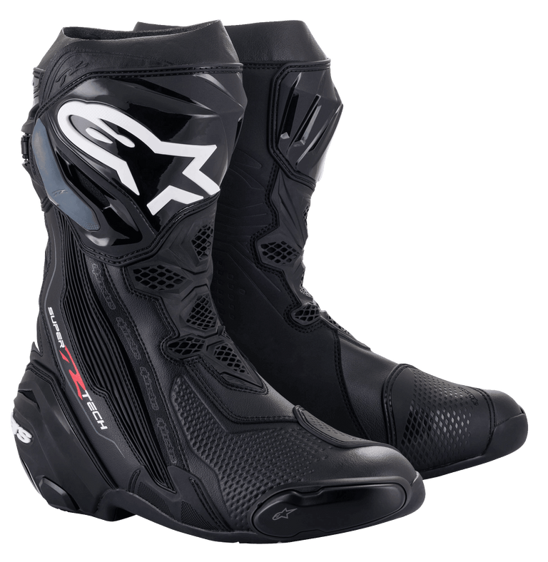 A black pair of Supertech R Boots from Alpinestars EU, showcasing white and silver detailing. These high-cut racing boots feature reinforced ankle, heel, and toe areas, with the brand's logo prominently displayed on the outer side of each boot for a sleek design.