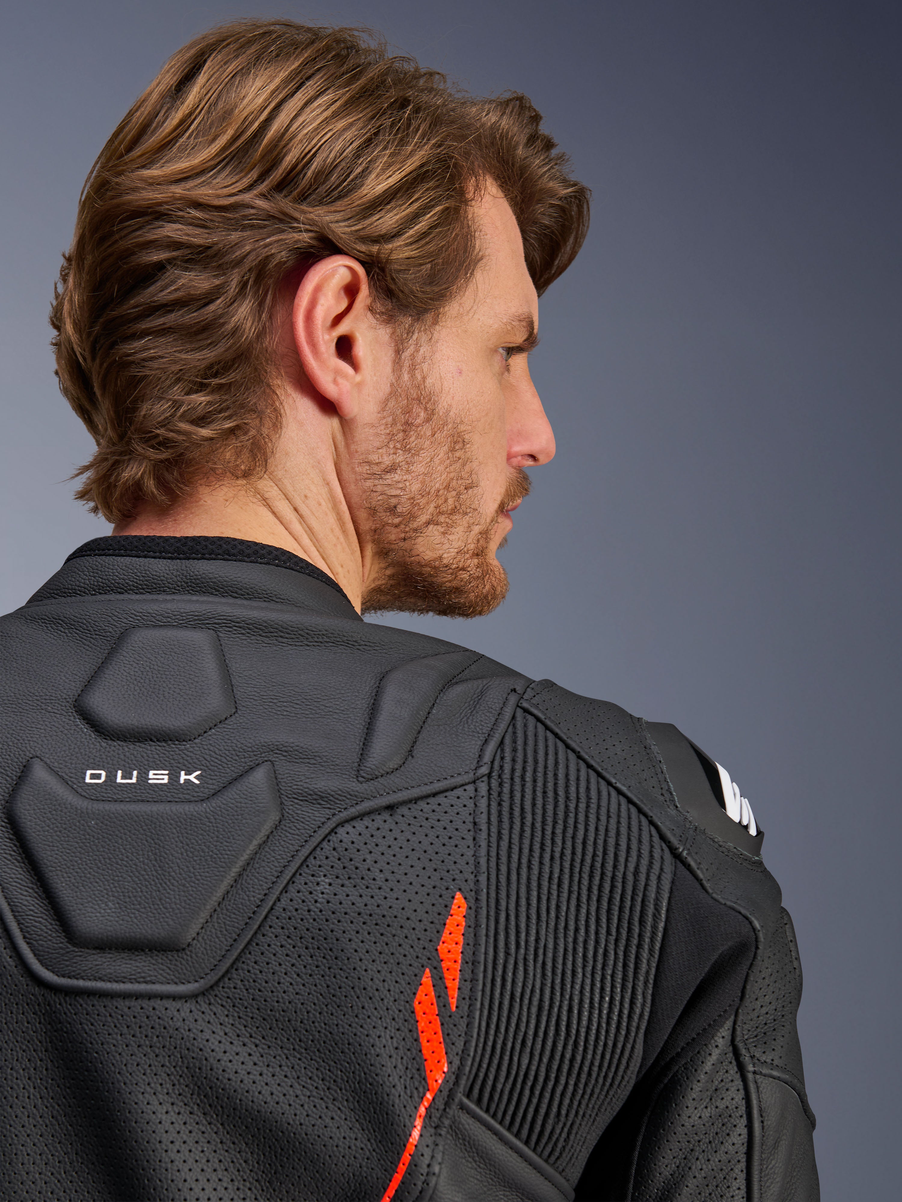 Giacca in pelle Alpinestars Dusk Airflow, Nero Rosso Fluo, primo piano della parte superiore della schiena e della spalla, con pelle traforata per la ventilazione e pannelli elastici a fisarmonica, dettaglio del marchio 'DUSK', indossata da un modello